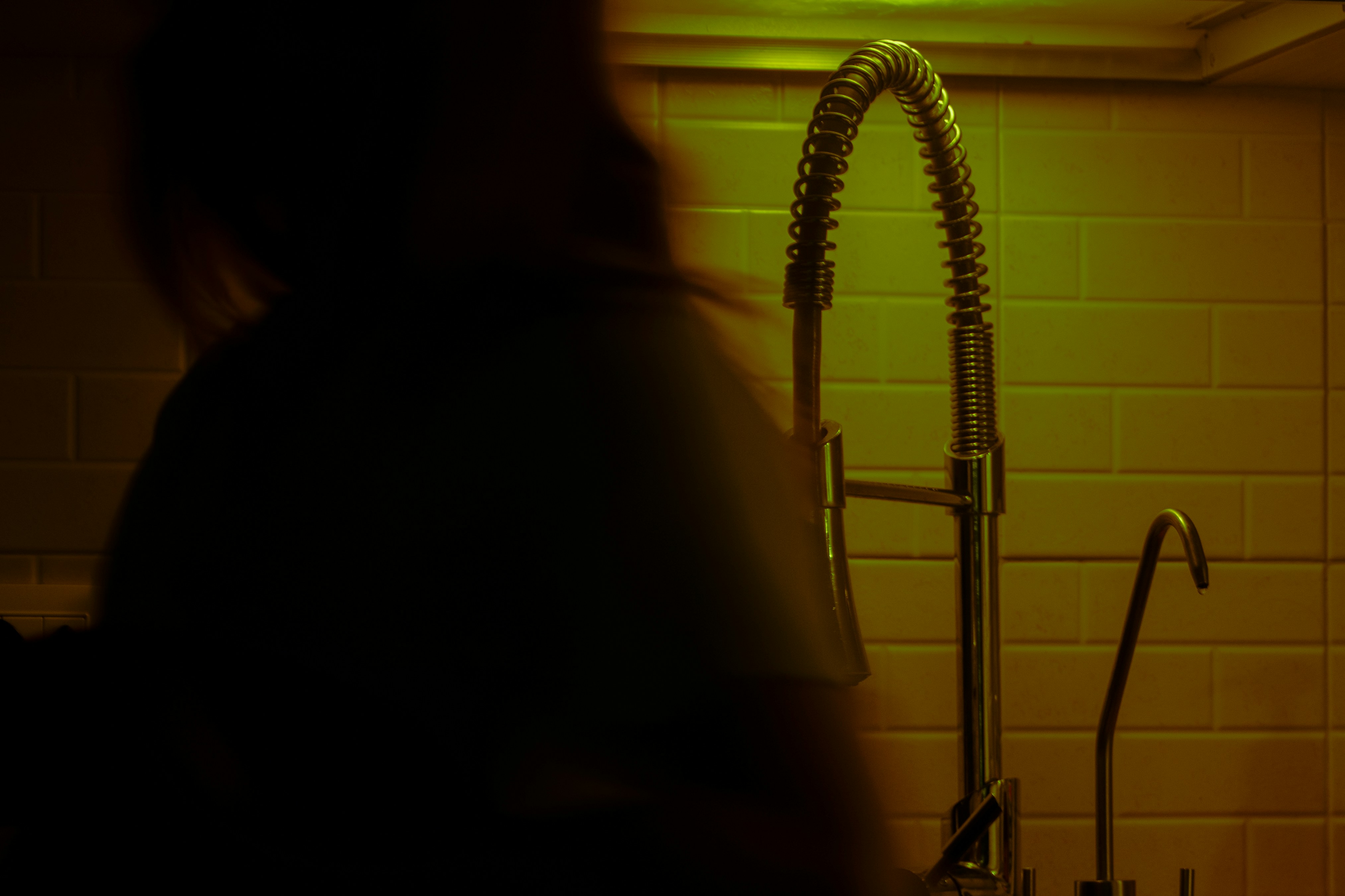 A kitchen faucet stands illuminated in low light.