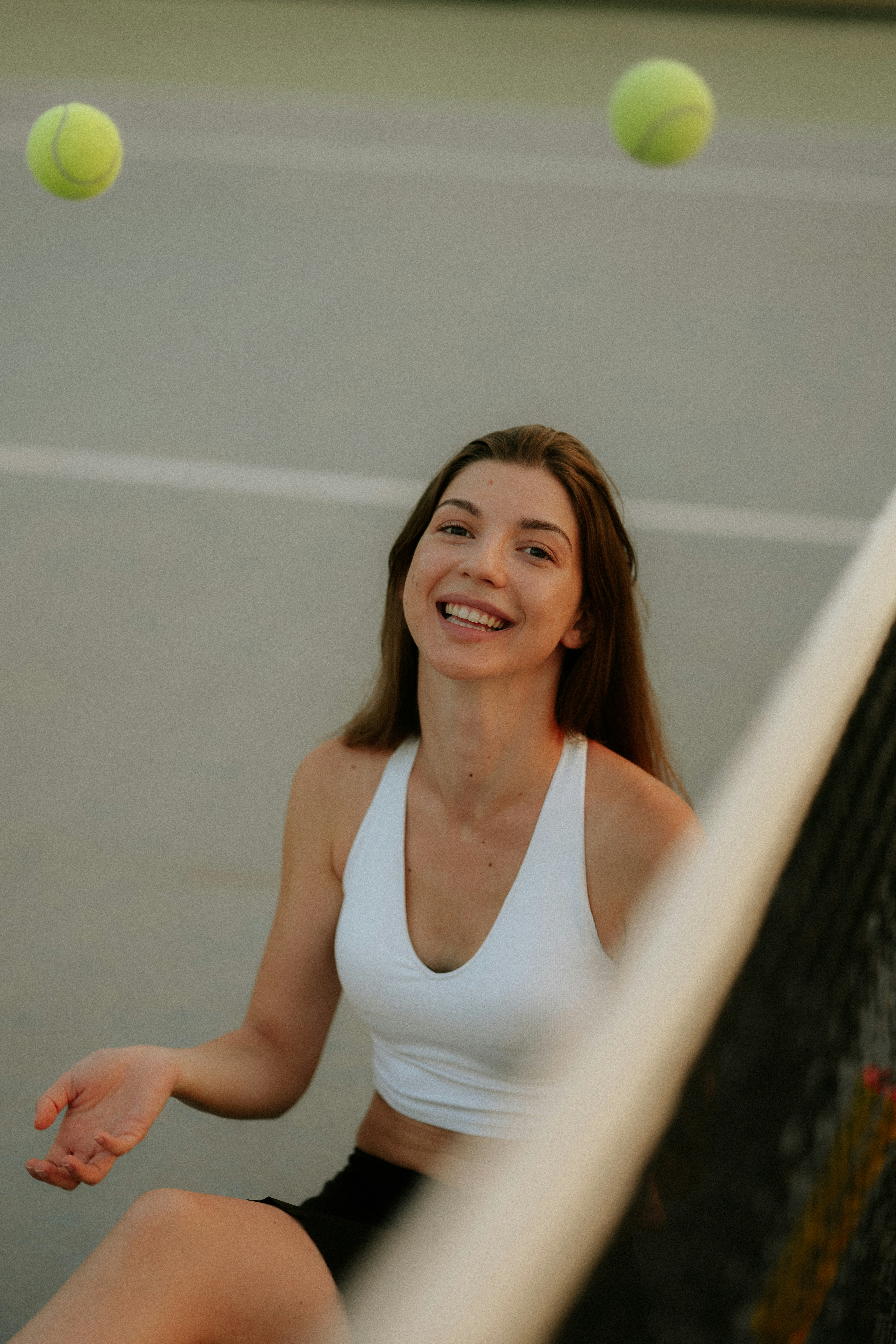 A woman smiles while juggling tennis balls.