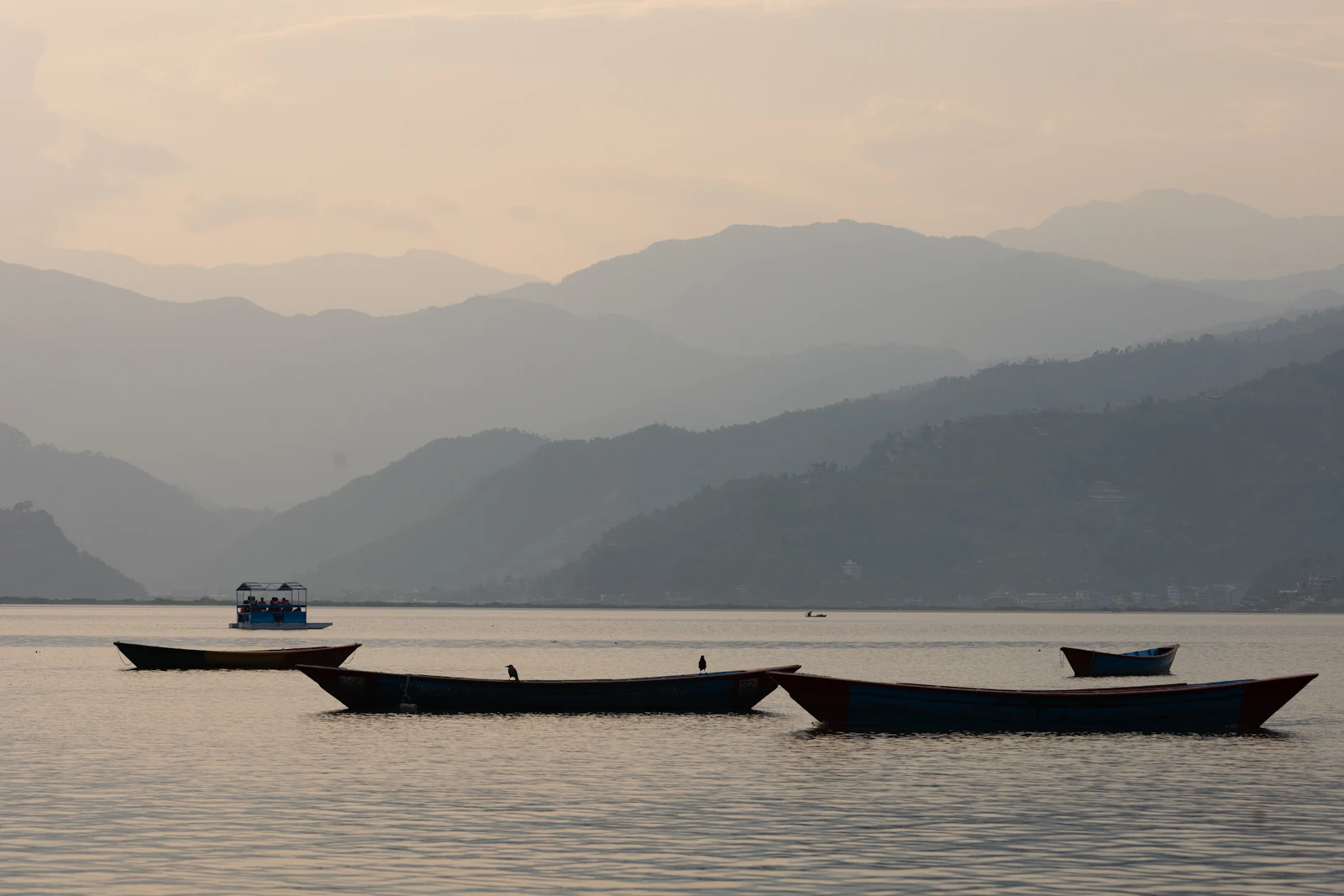 Wooden rowing boats resting on Phewa Lake in Pokhara, forested hills fading into haze behind
