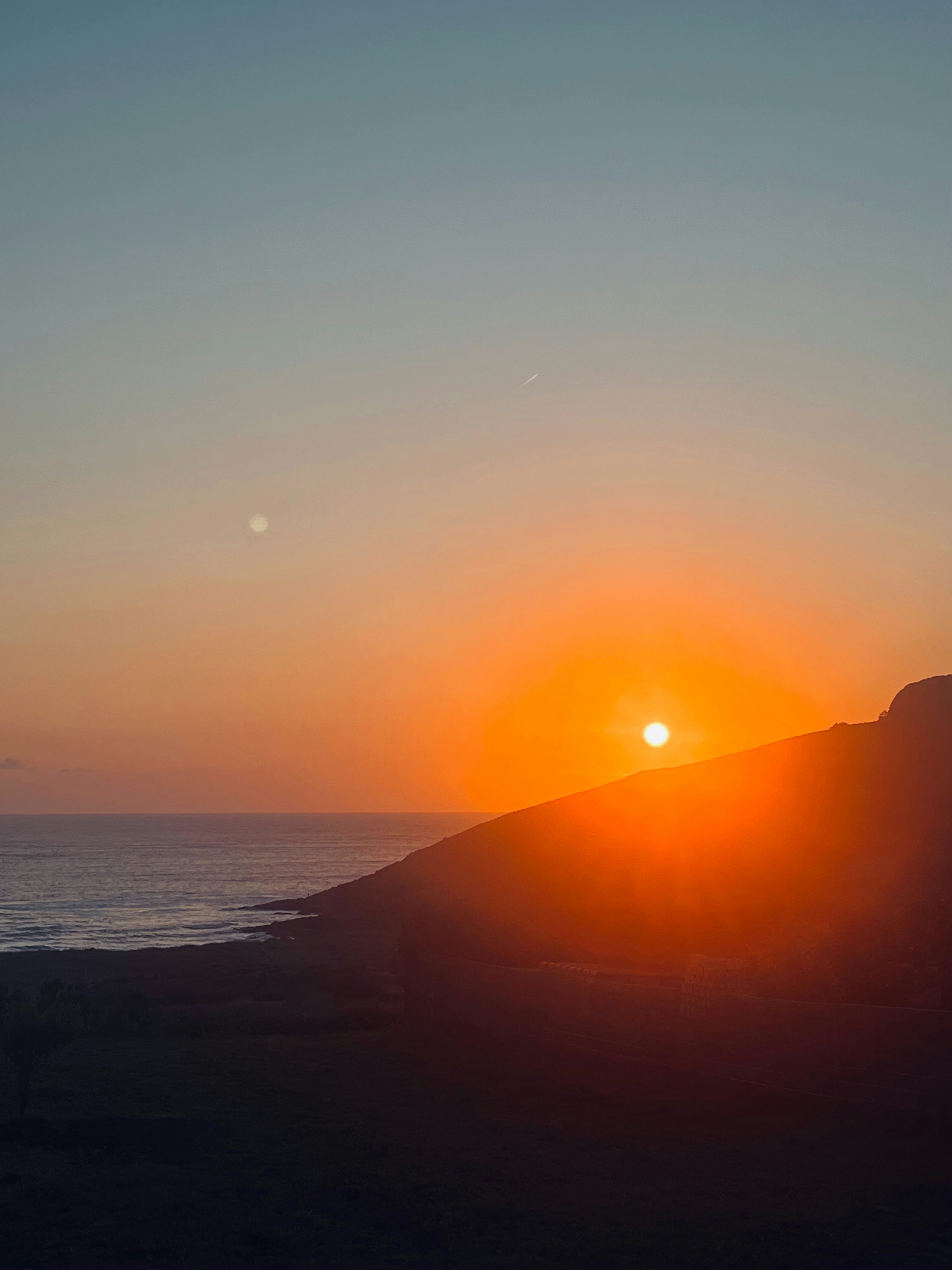 A sunset over the ocean and a hill.