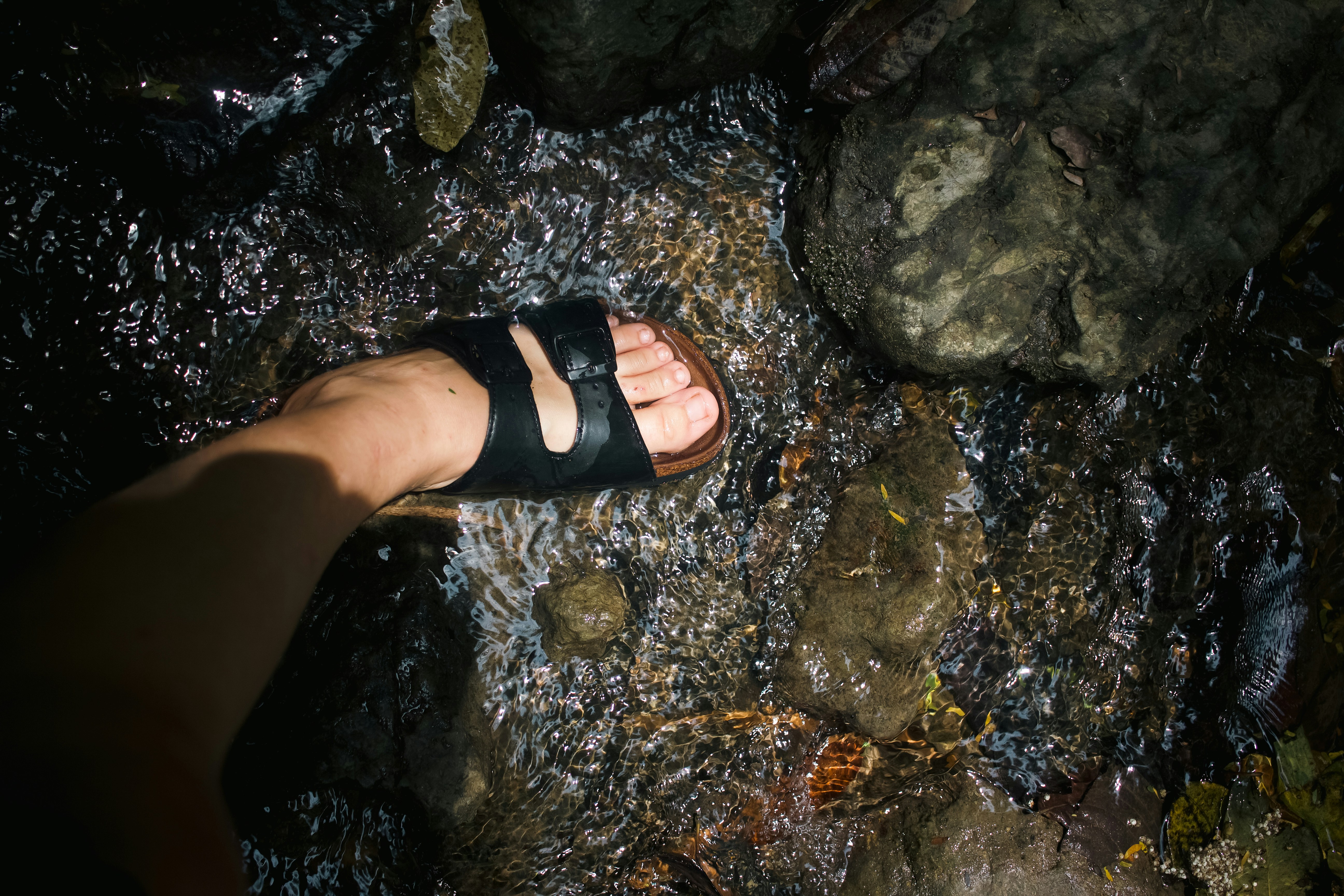Mit dem Fuß in Sandalen geht es durch einen Bach