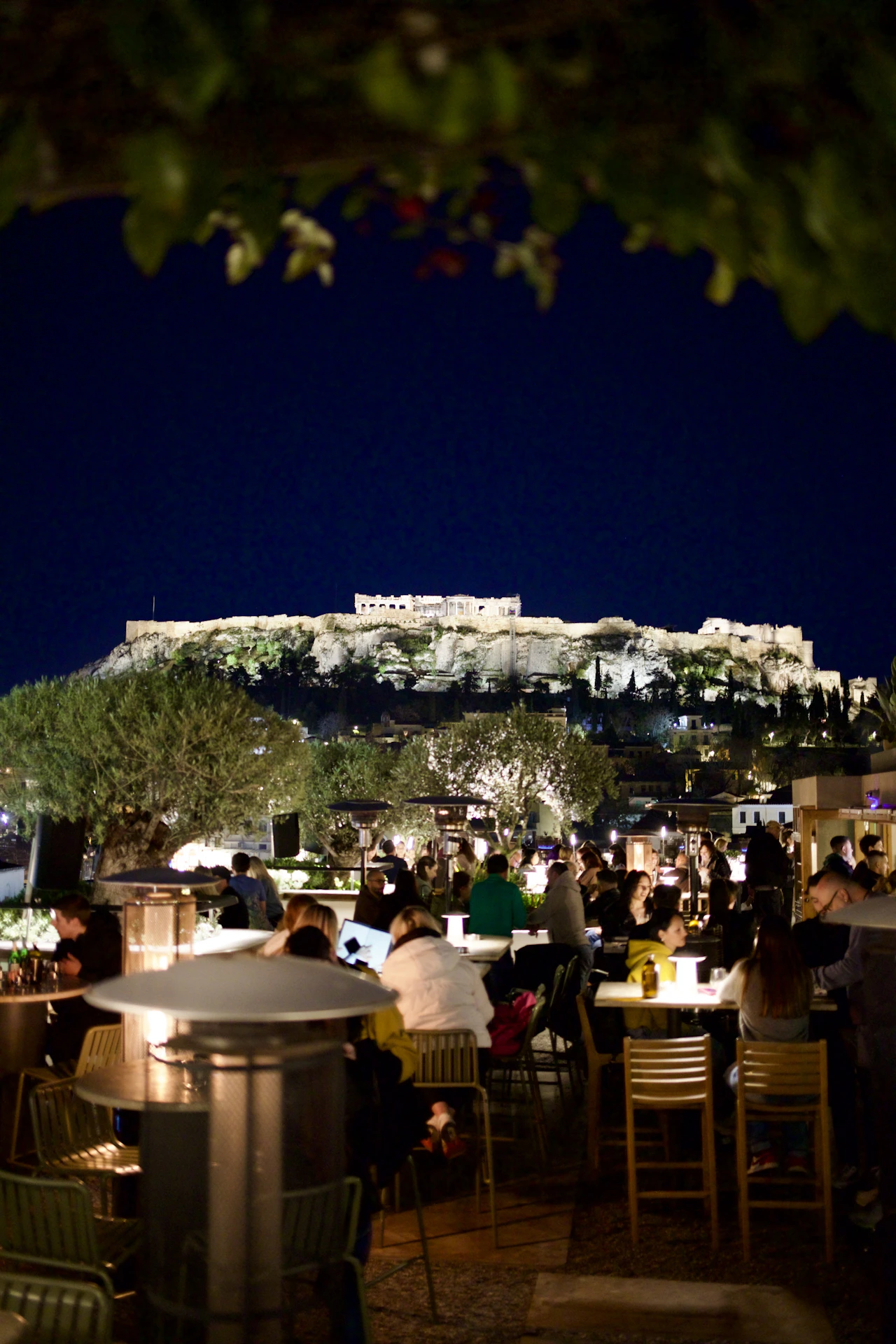 People dining at night with the floodlit Acropolis behind