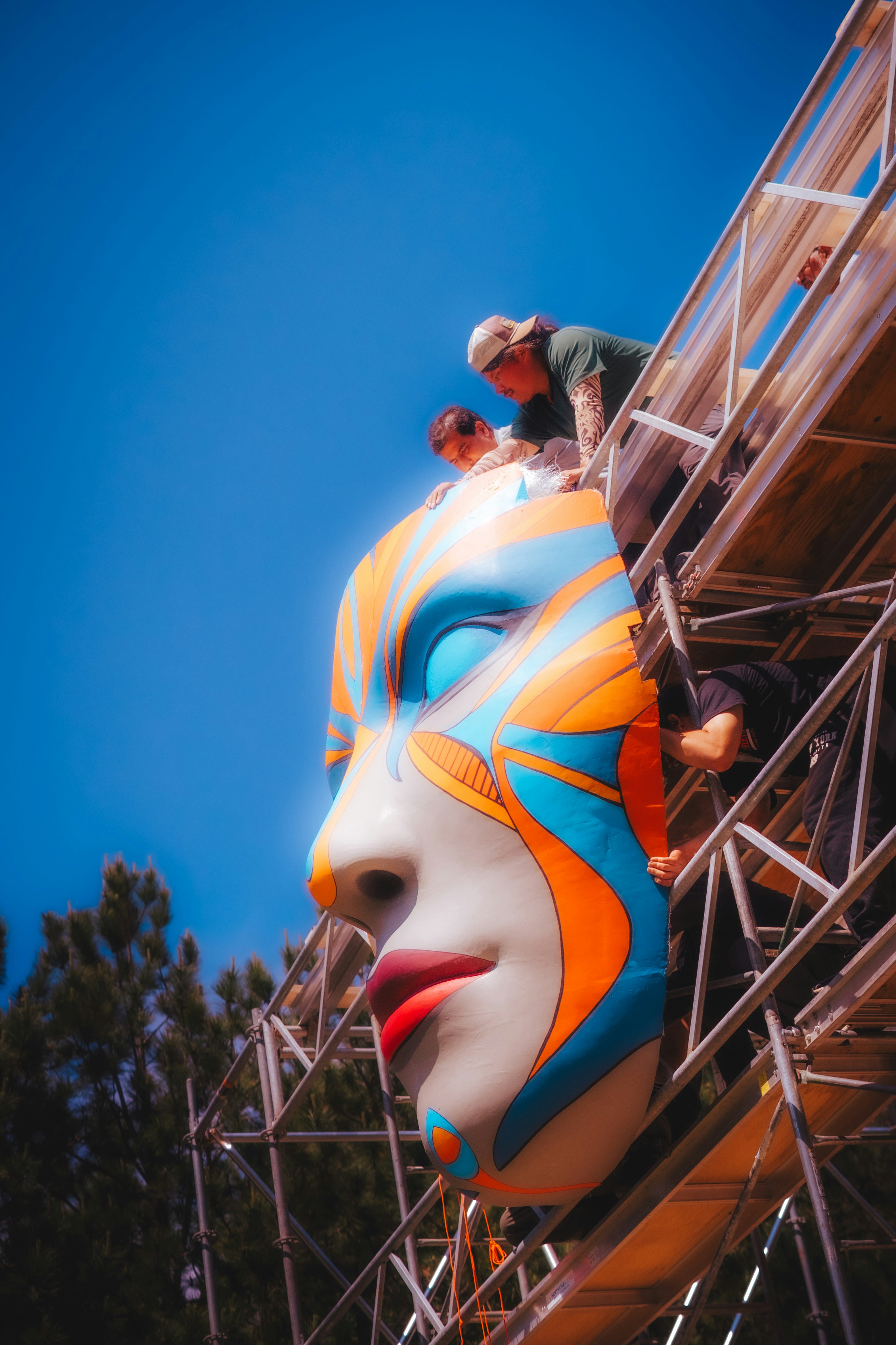 People work on a giant colorful face sculpture.