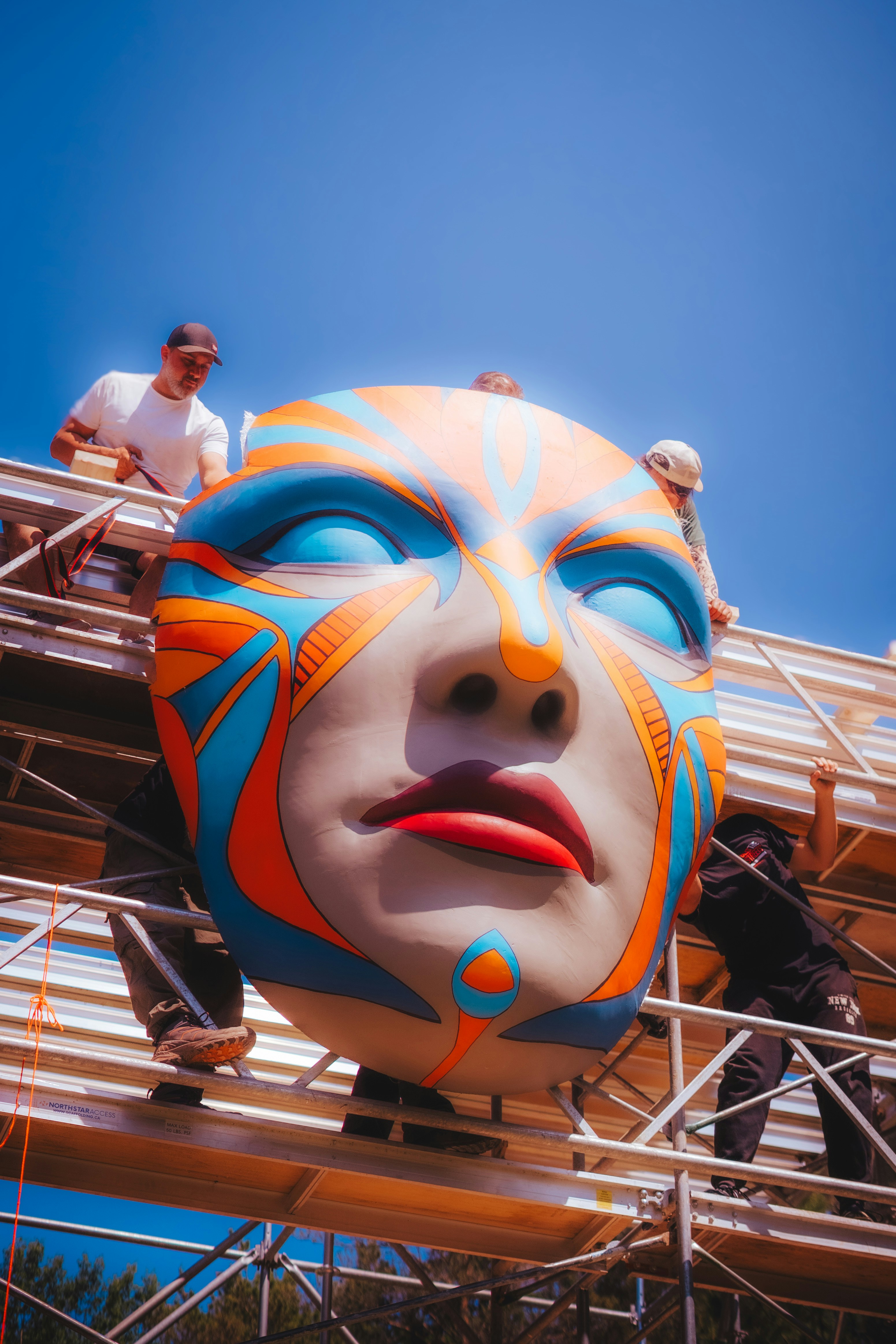 Workers install a massive, colorful face sculpture.