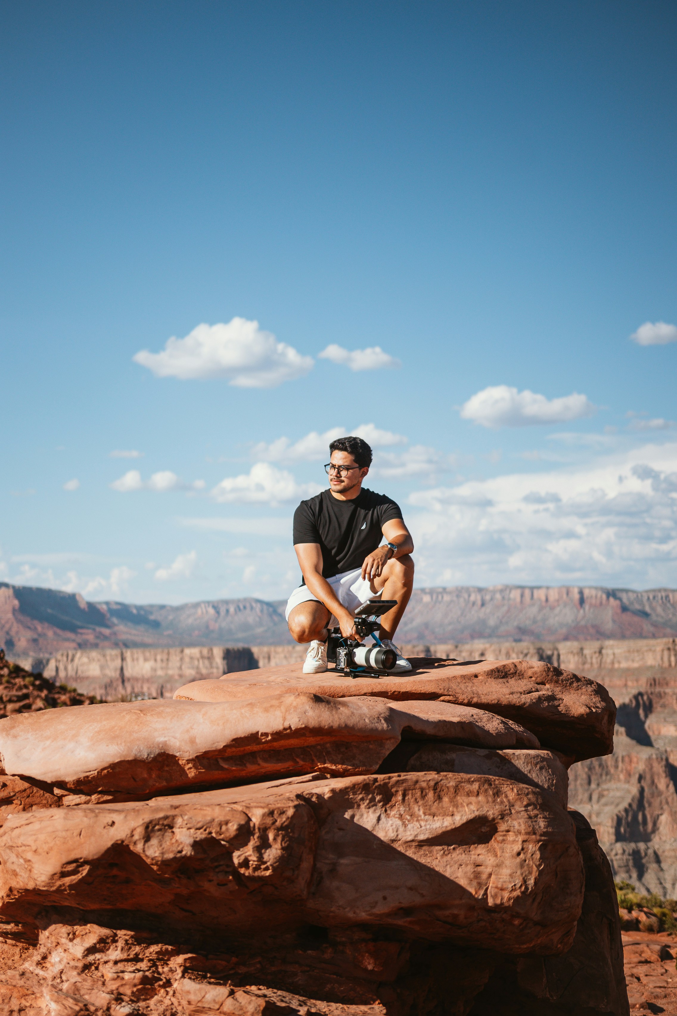 Man crouches on a rock, overlooking a canyon.