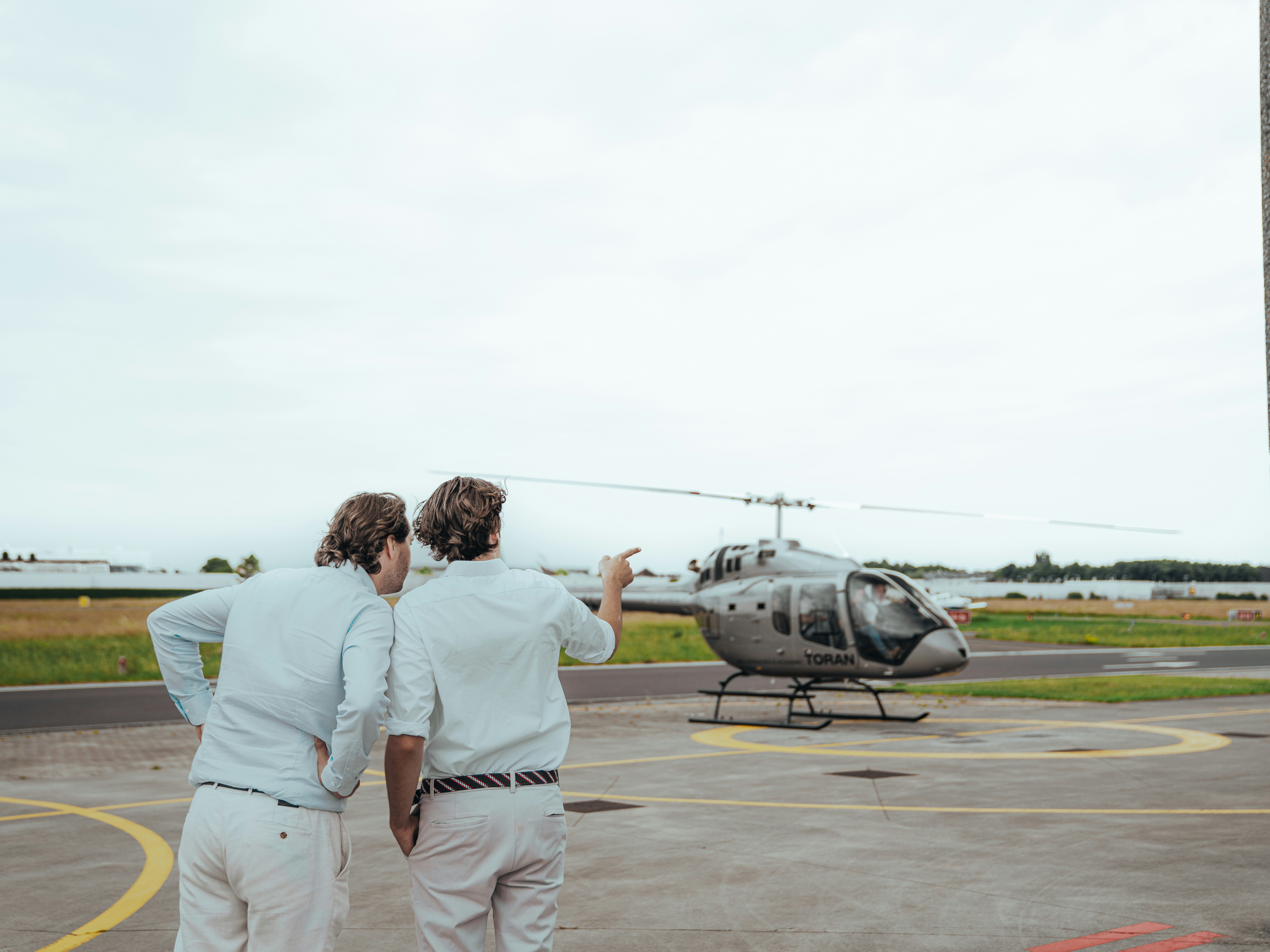 Two people look at a helicopter on a helipad.