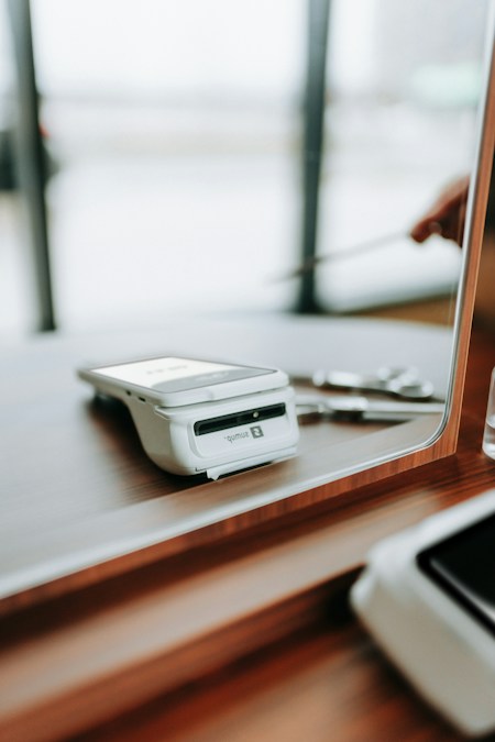 Un terminal de paiement électronique blanc posé sur un comptoir en bois, devant une vitre