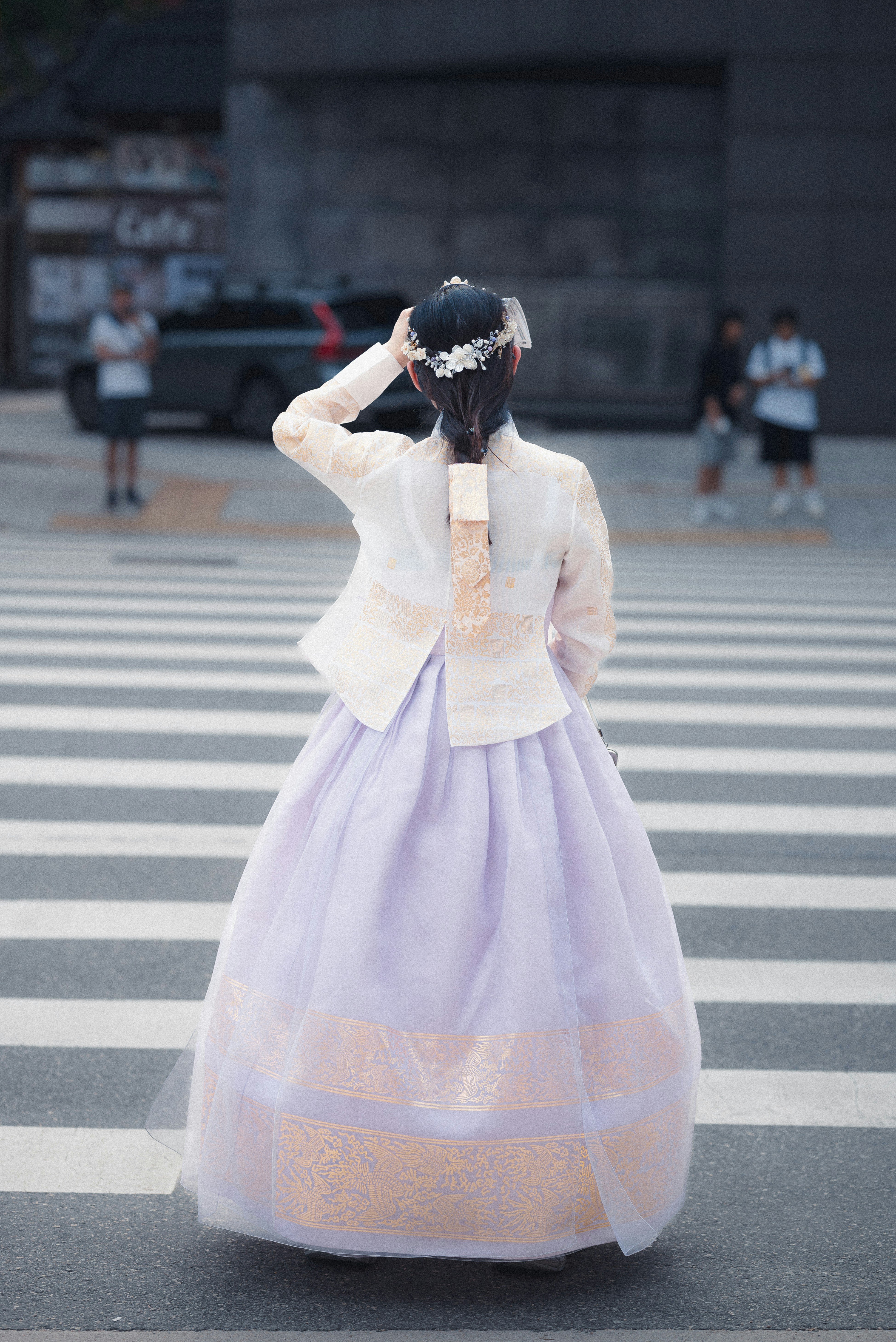 A woman in traditional korean clothing crosses the street.