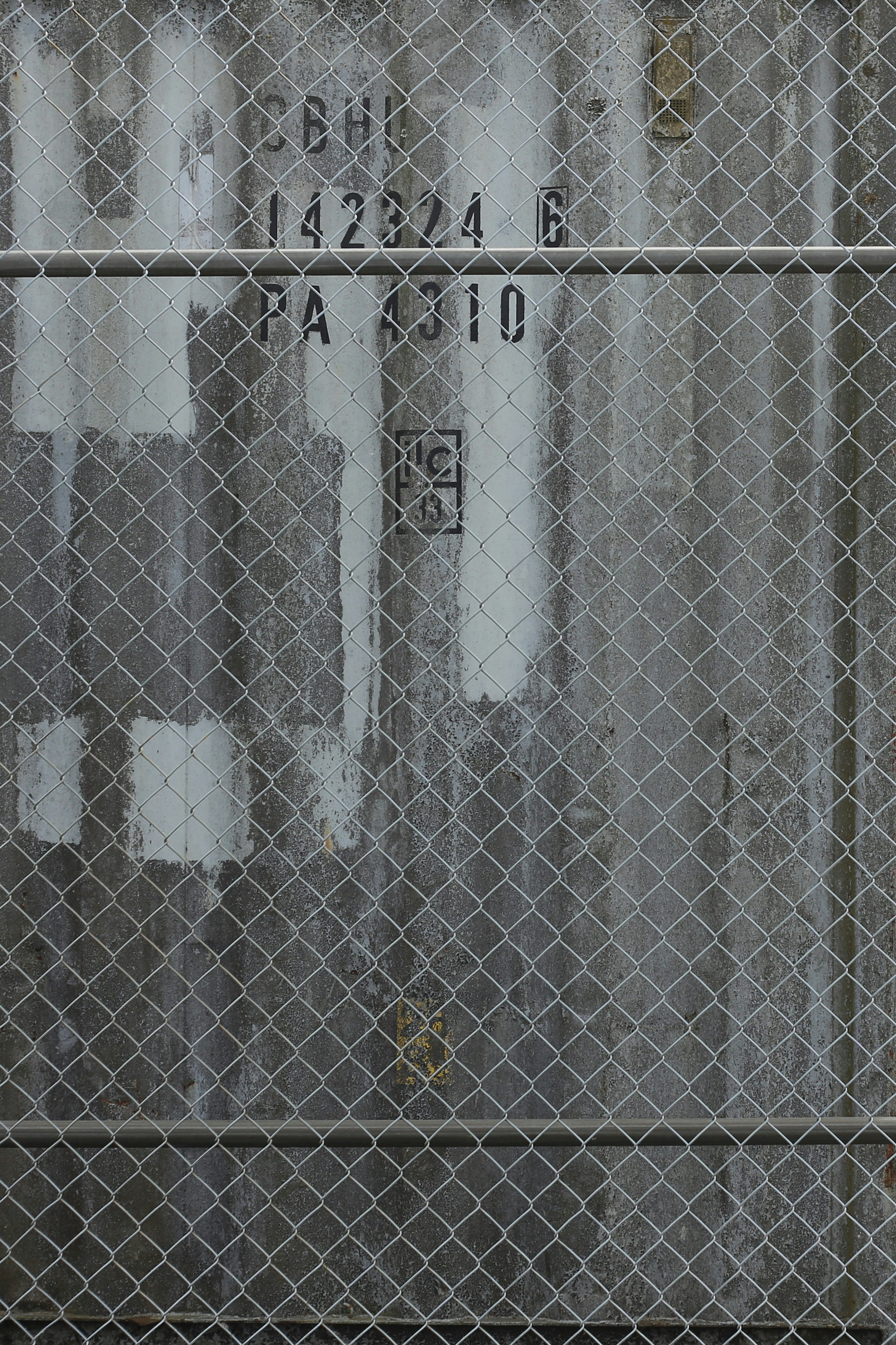 Recinzione a maglie di catena davanti alle marcature industriali.