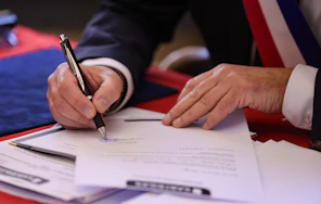 A person signs a document with a pen.