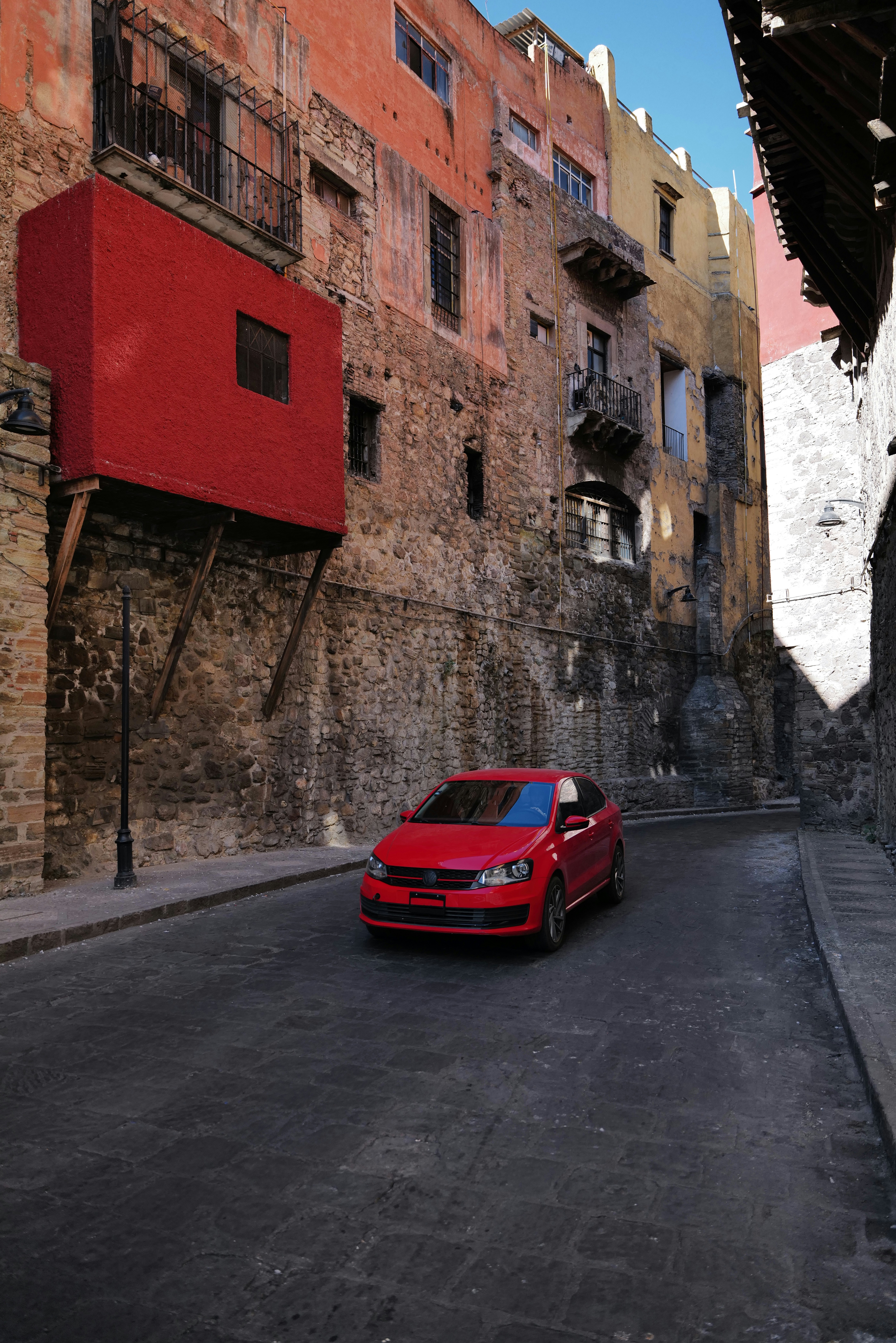Red car driving down a narrow, cobblestone street.