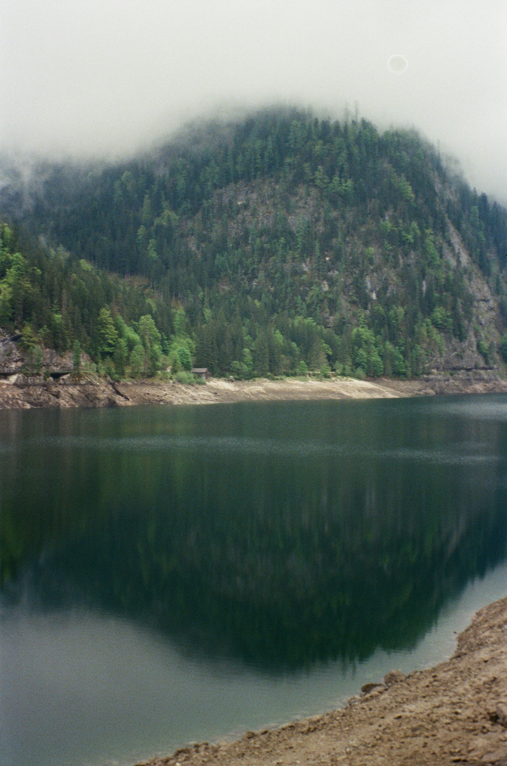 Fog-shrouded mountain reflected in the still lake water.