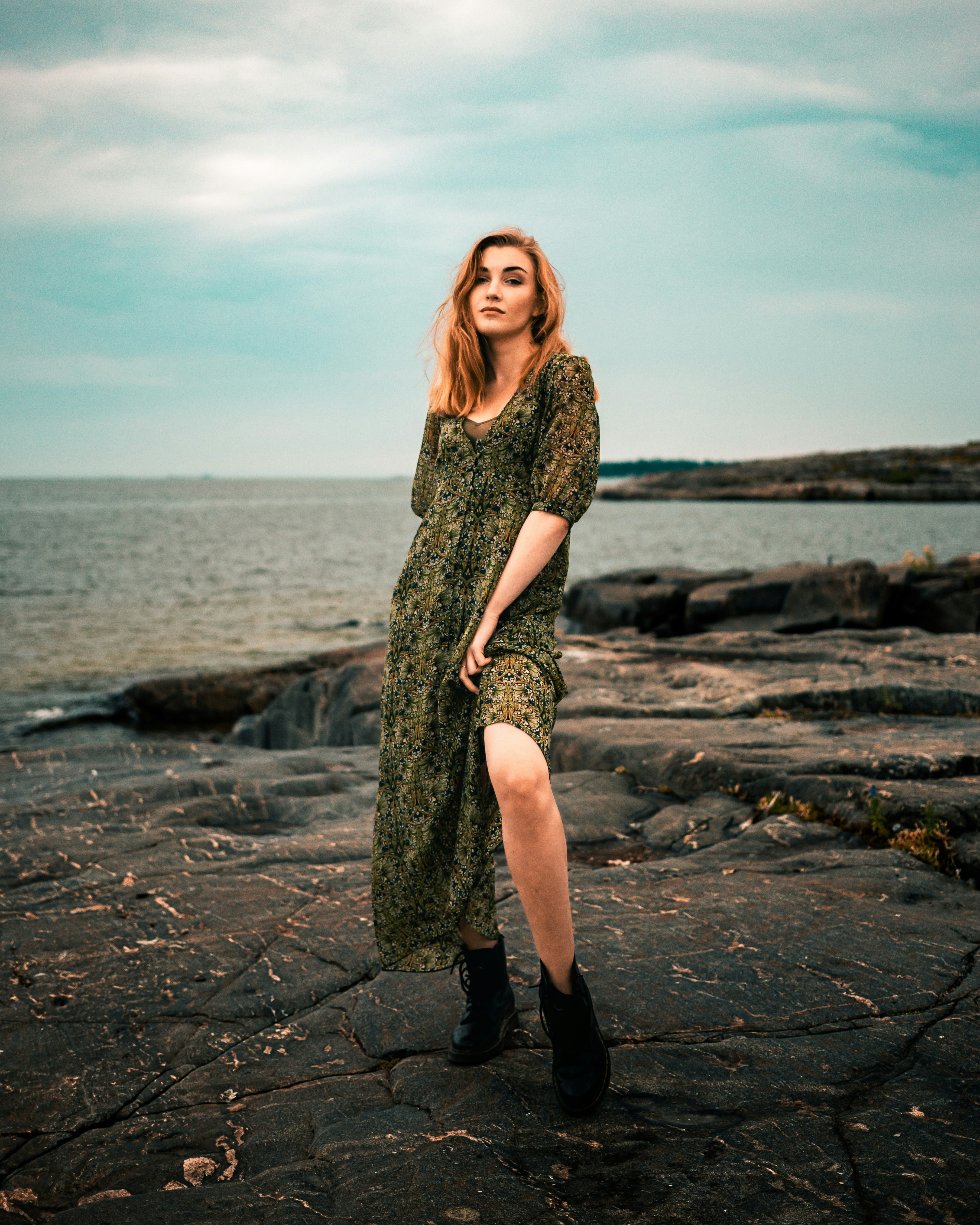 A woman stands by the sea in a dress