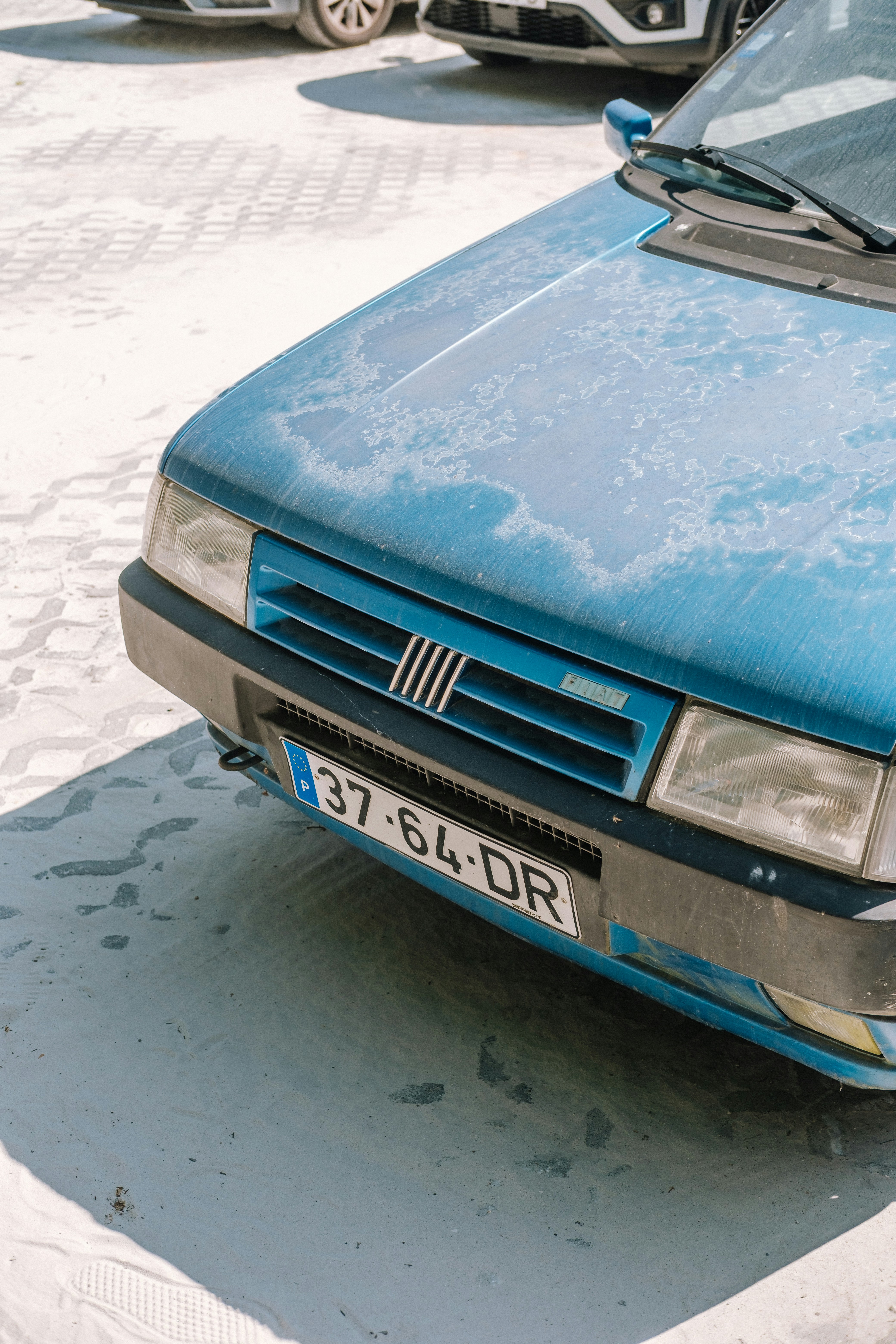 Blue fiat uno parked on a sandy surface.