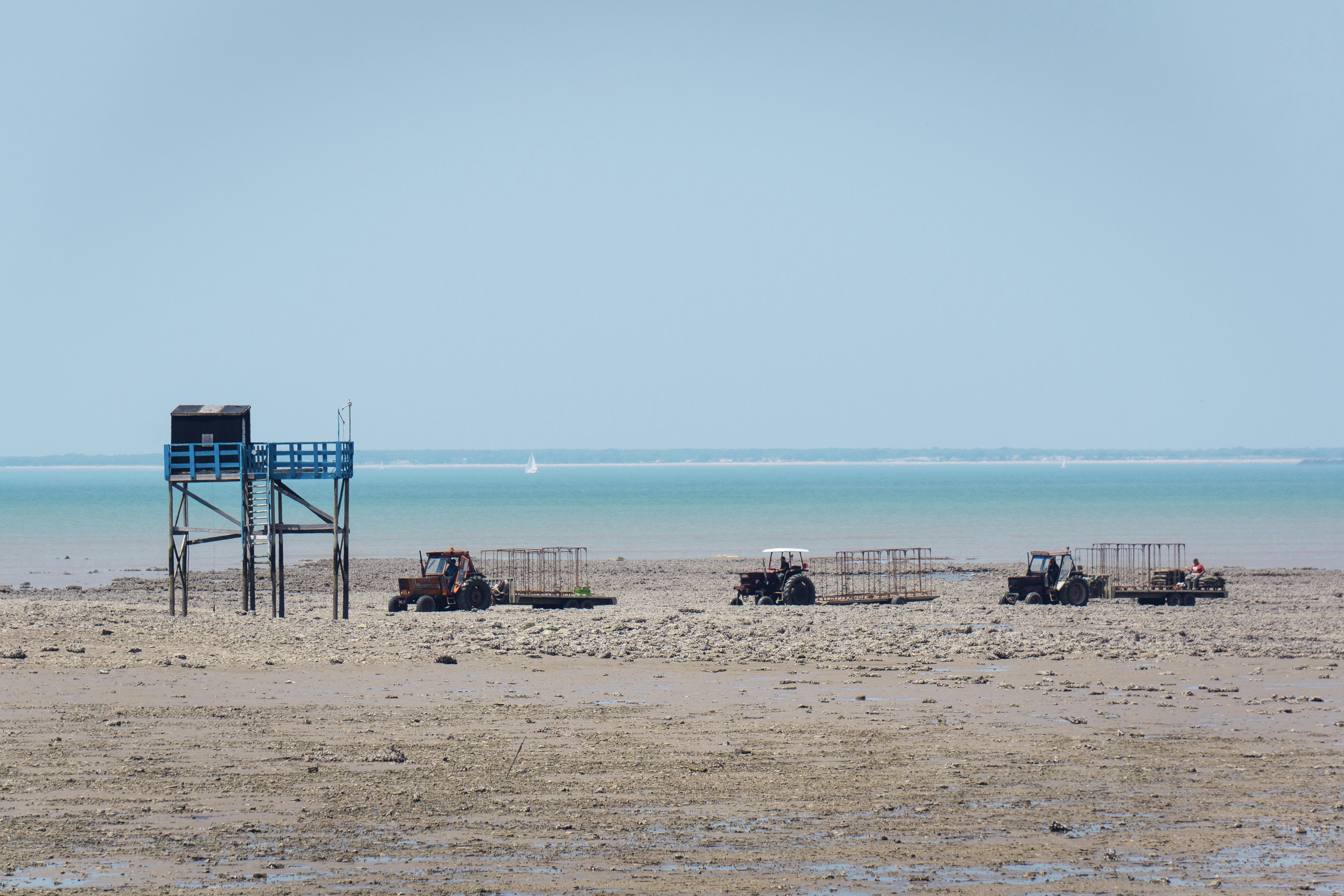 Tractors and a tower are on the sandy shore.