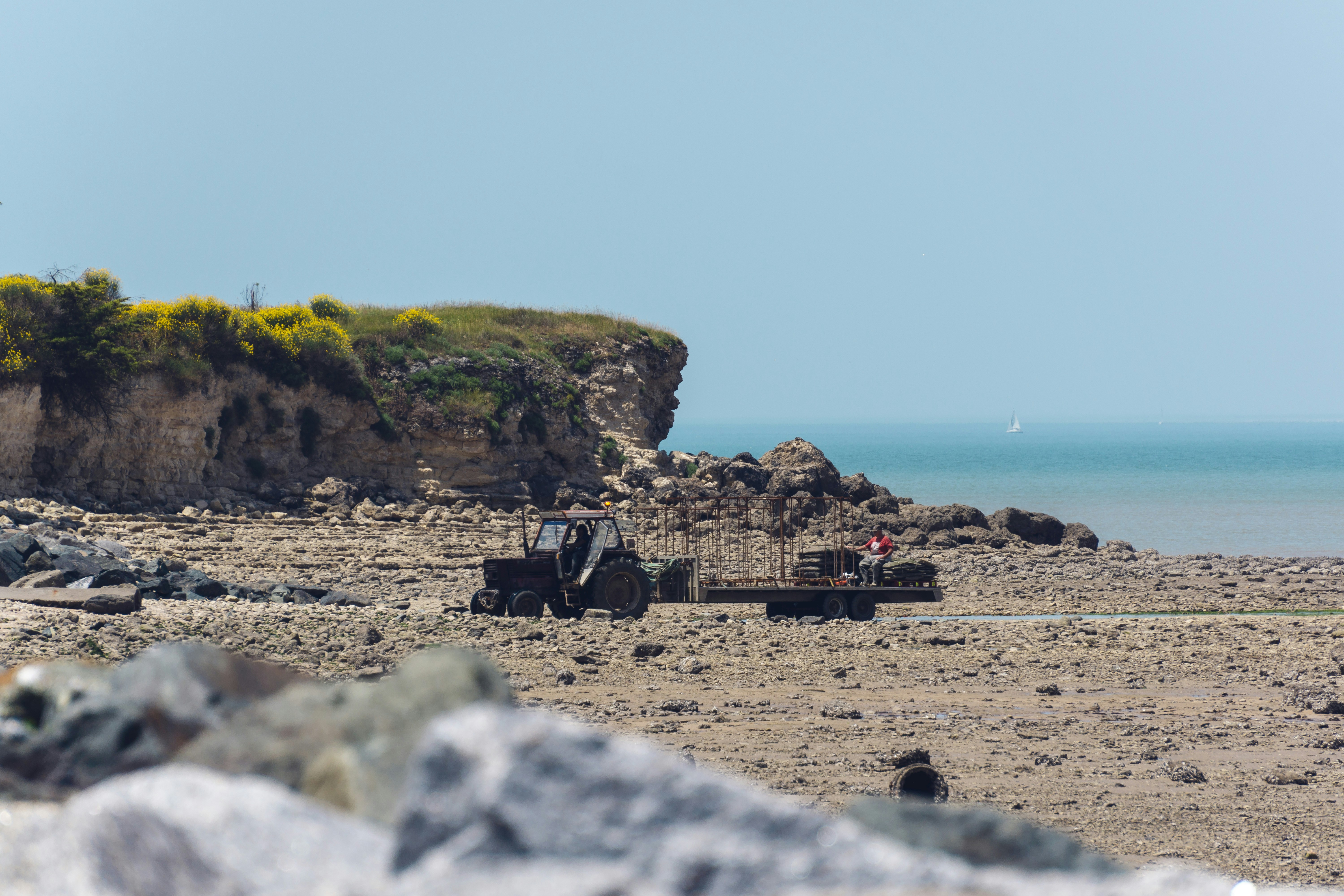 A tractor hauls a load along the rocky shore.