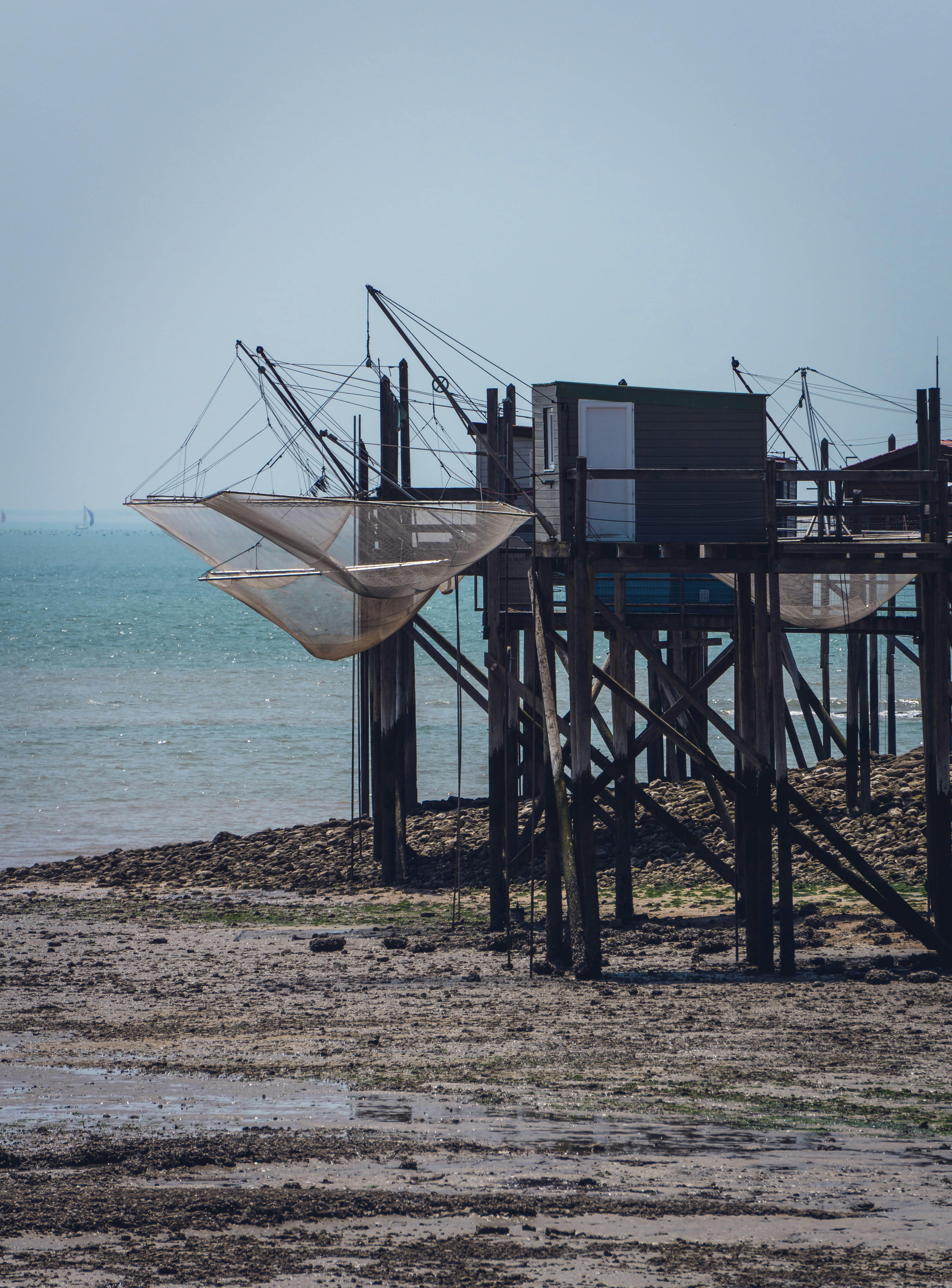Fishing structures stand on a sandy shore by the sea.