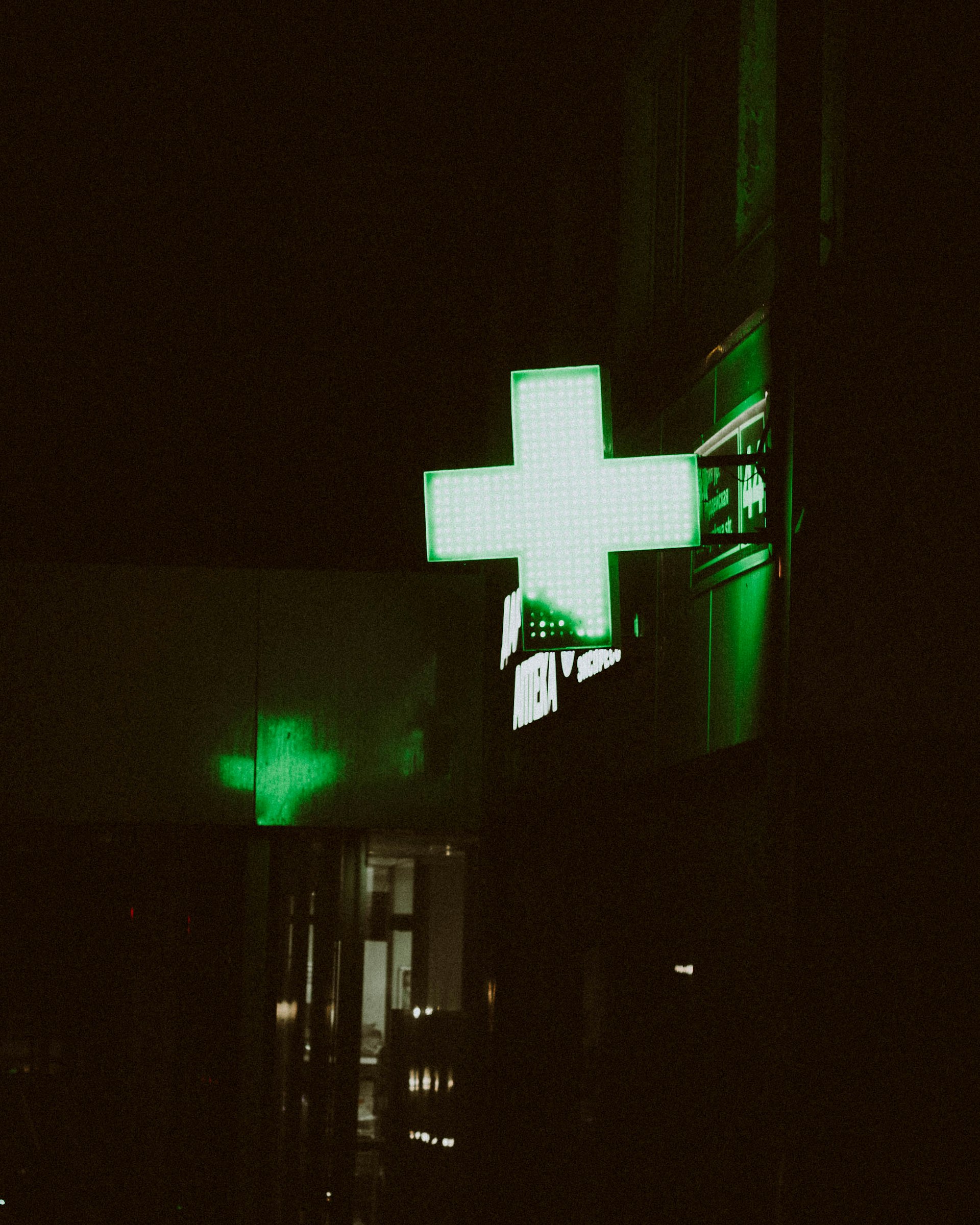 A pharmacy sign glows green at night.