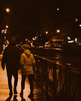 Two people walk down a wet street at night.