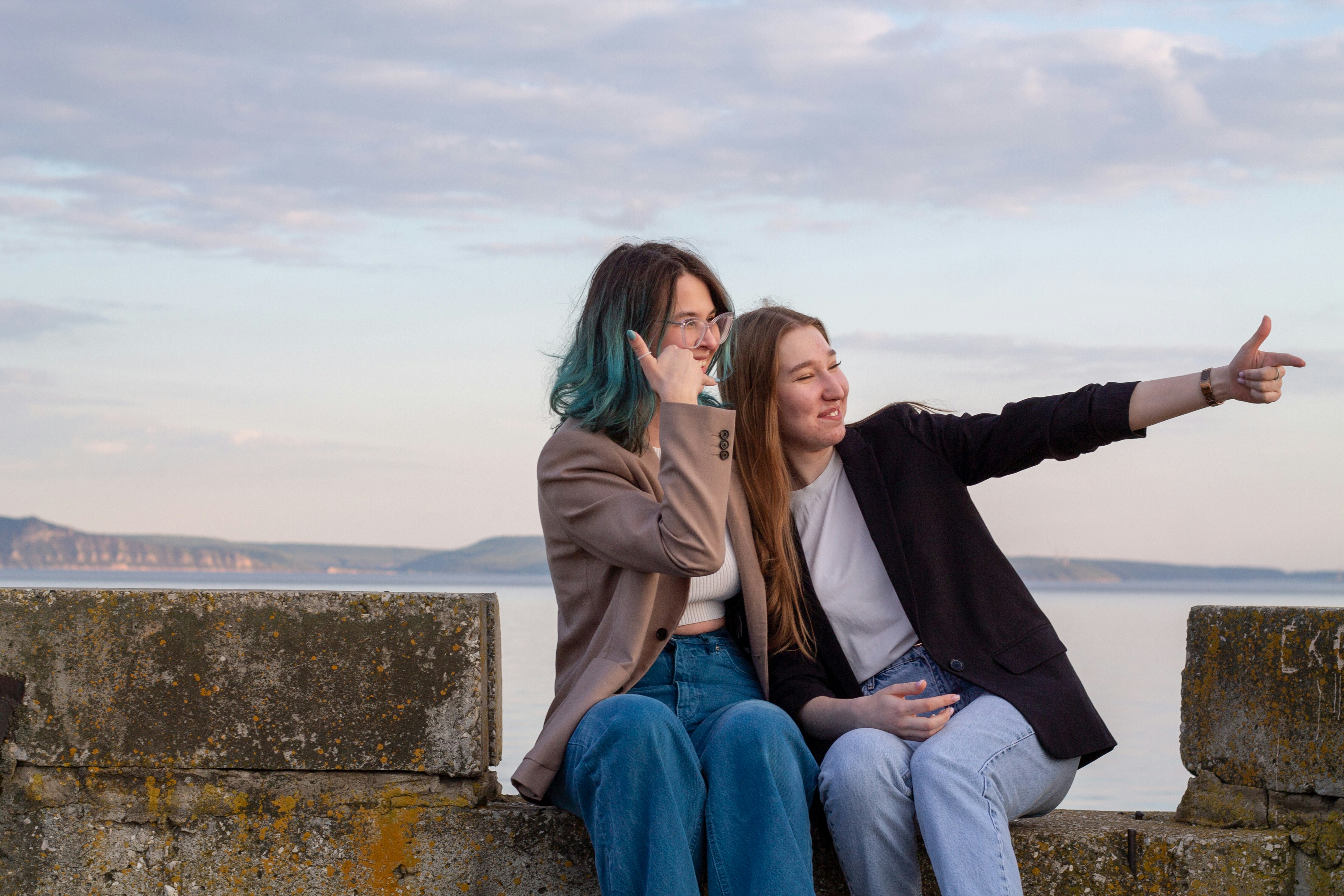 Zwei Frauen sitzen auf einer Mauer am Meer