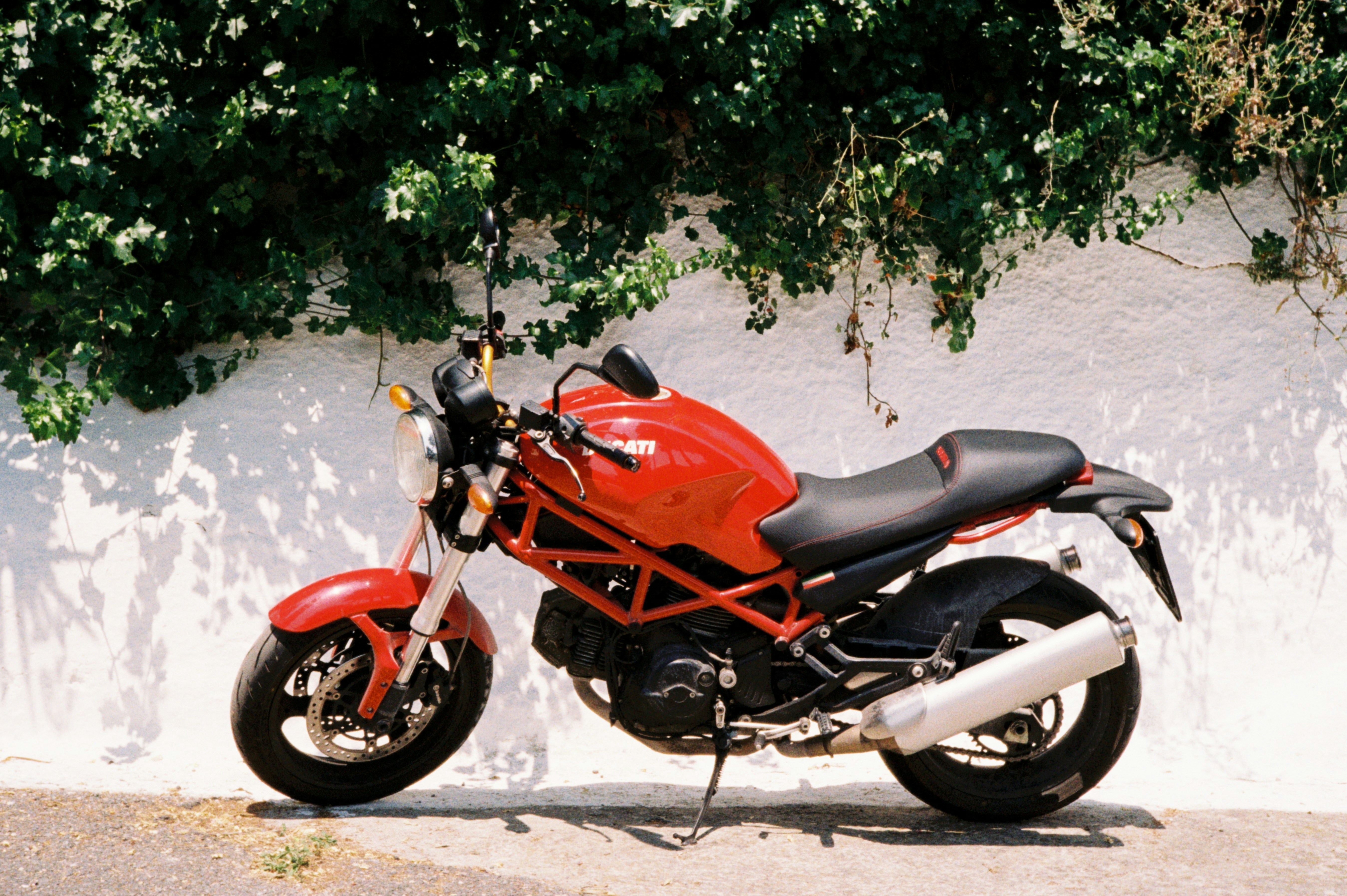 A red motorcycle is parked against a white wall.