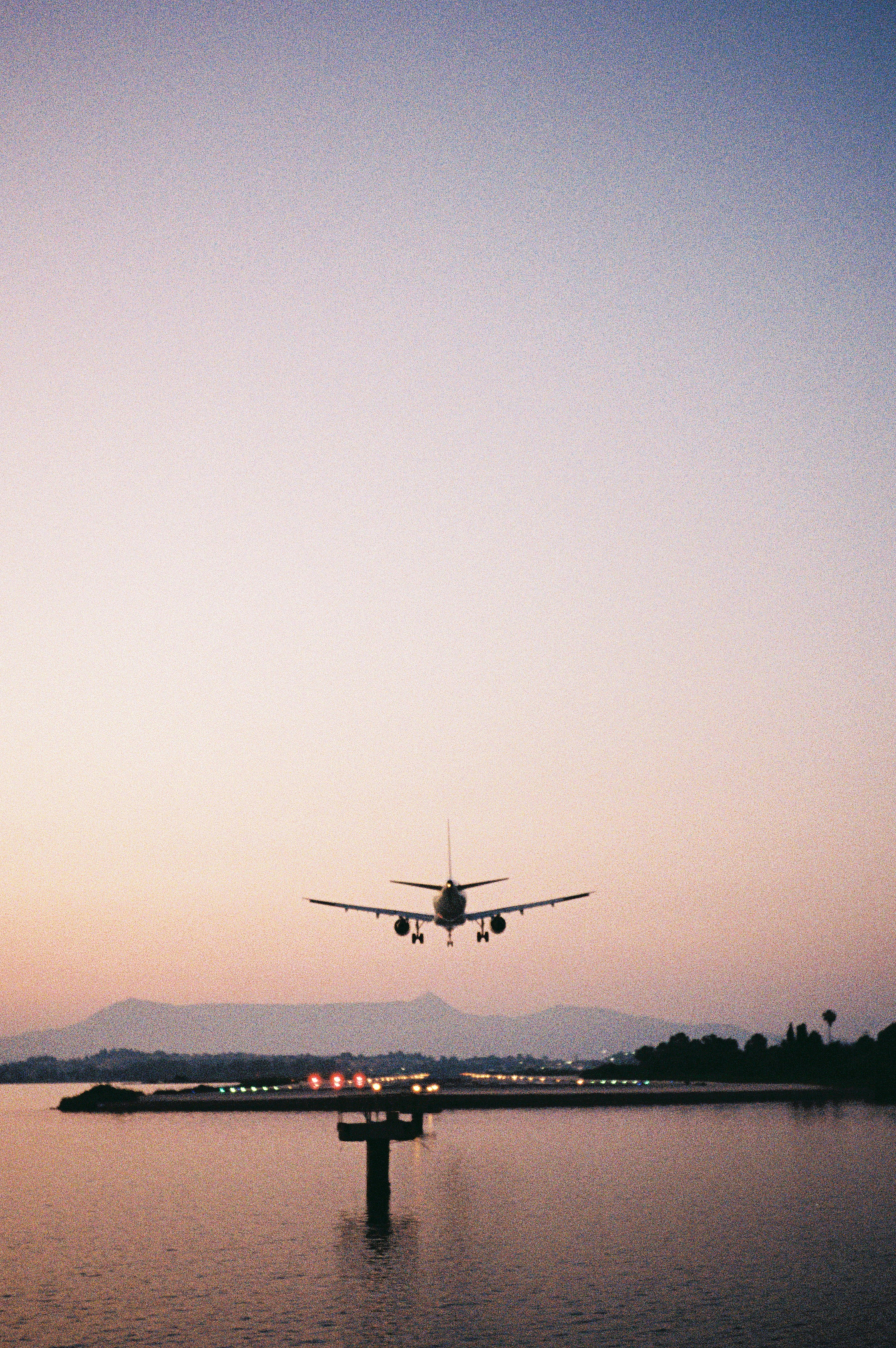 An airplane is landing over the water at sunset.