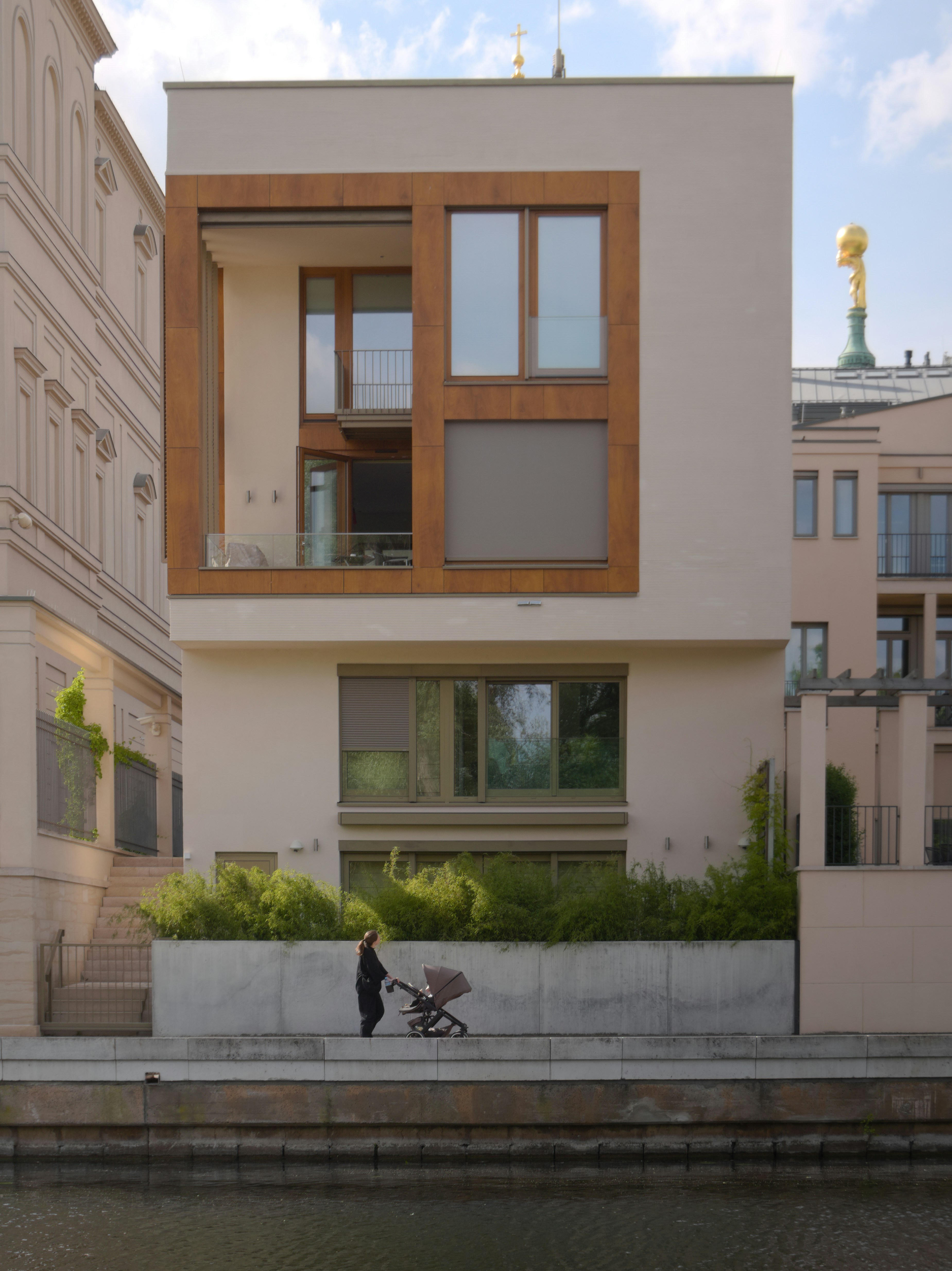 A pale house with a deep timber-framed window above a planted terrace by the water