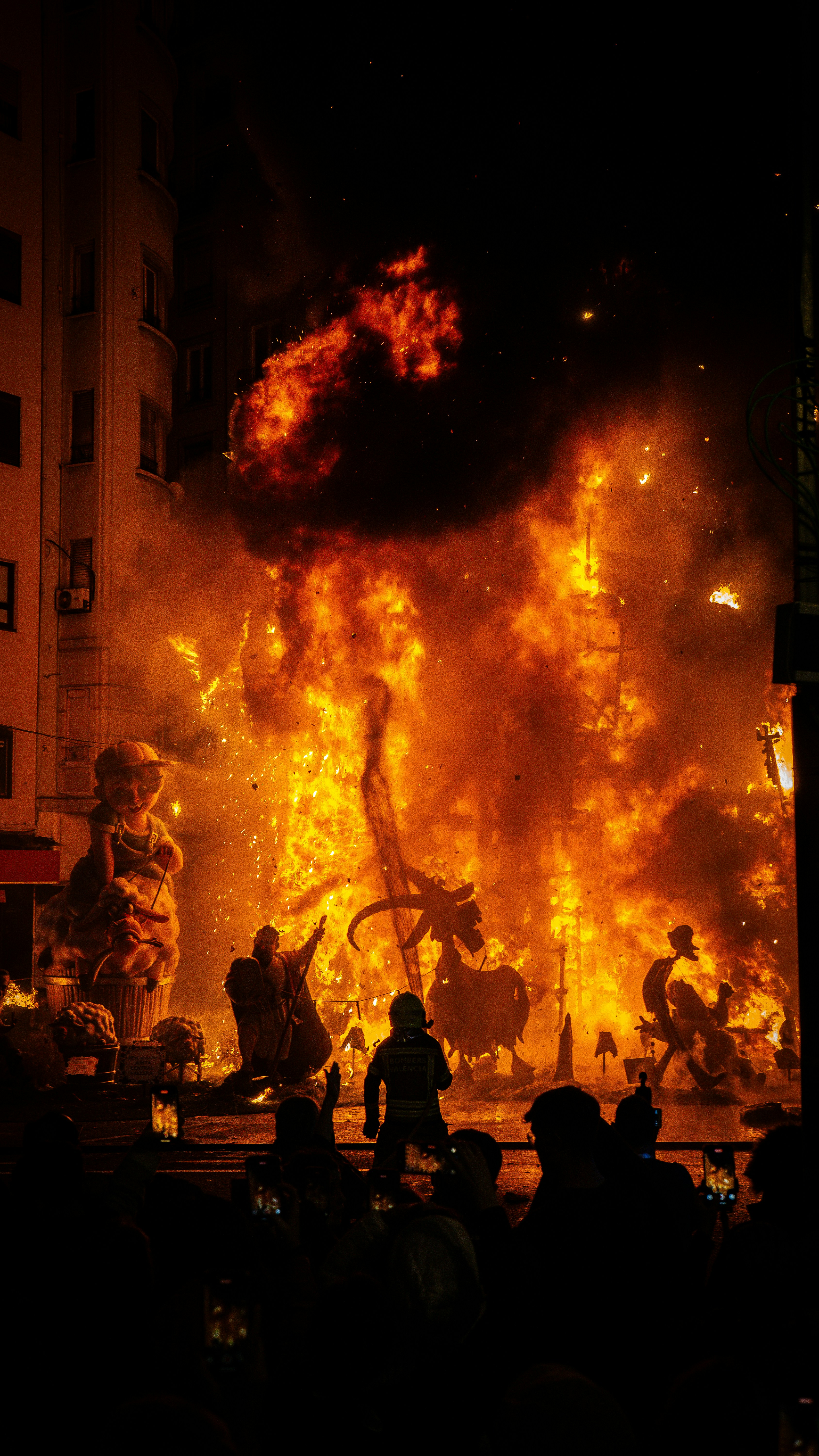 A burning structure with people watching the blaze.