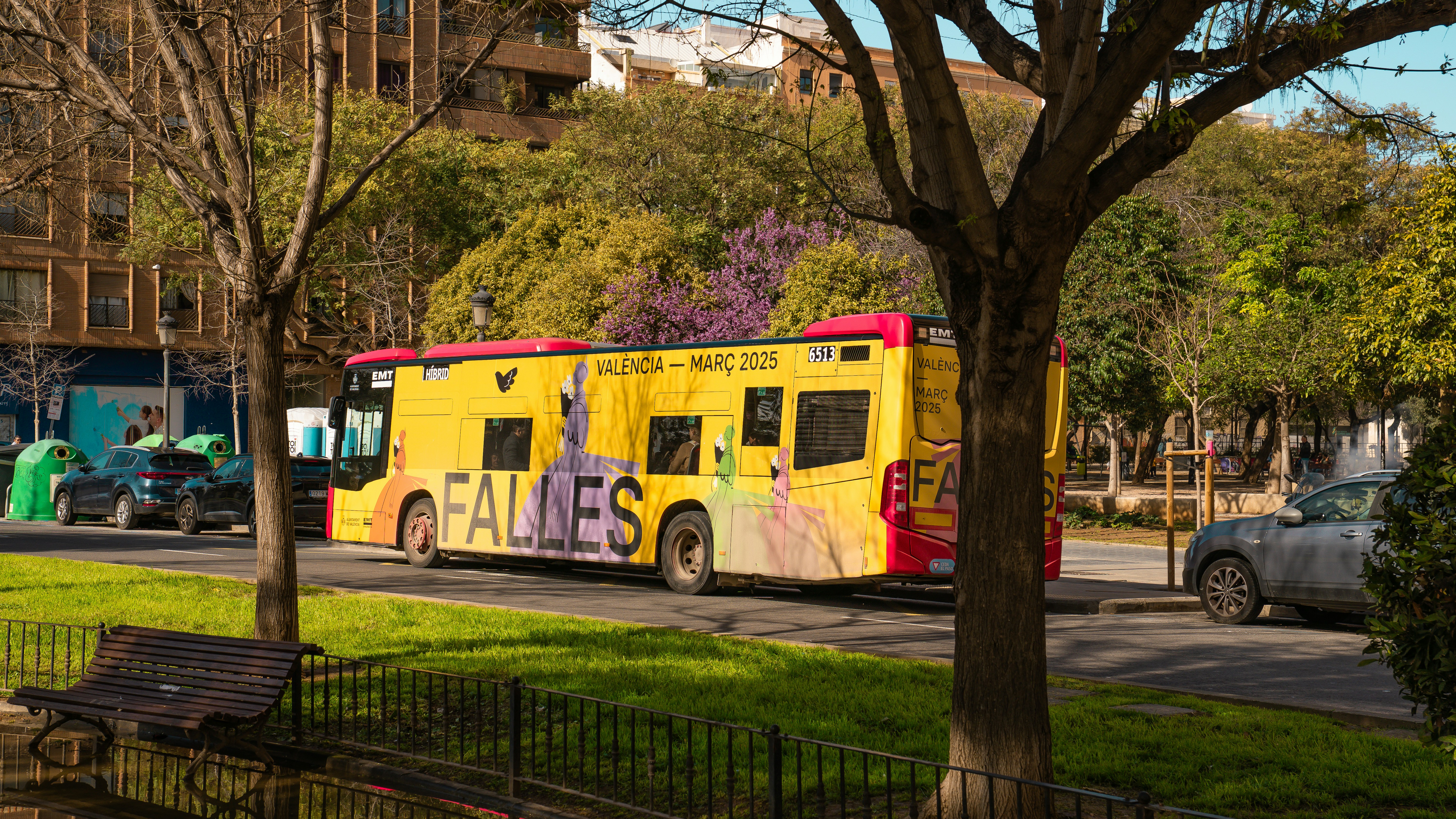 A yellow bus is parked near trees in a city.