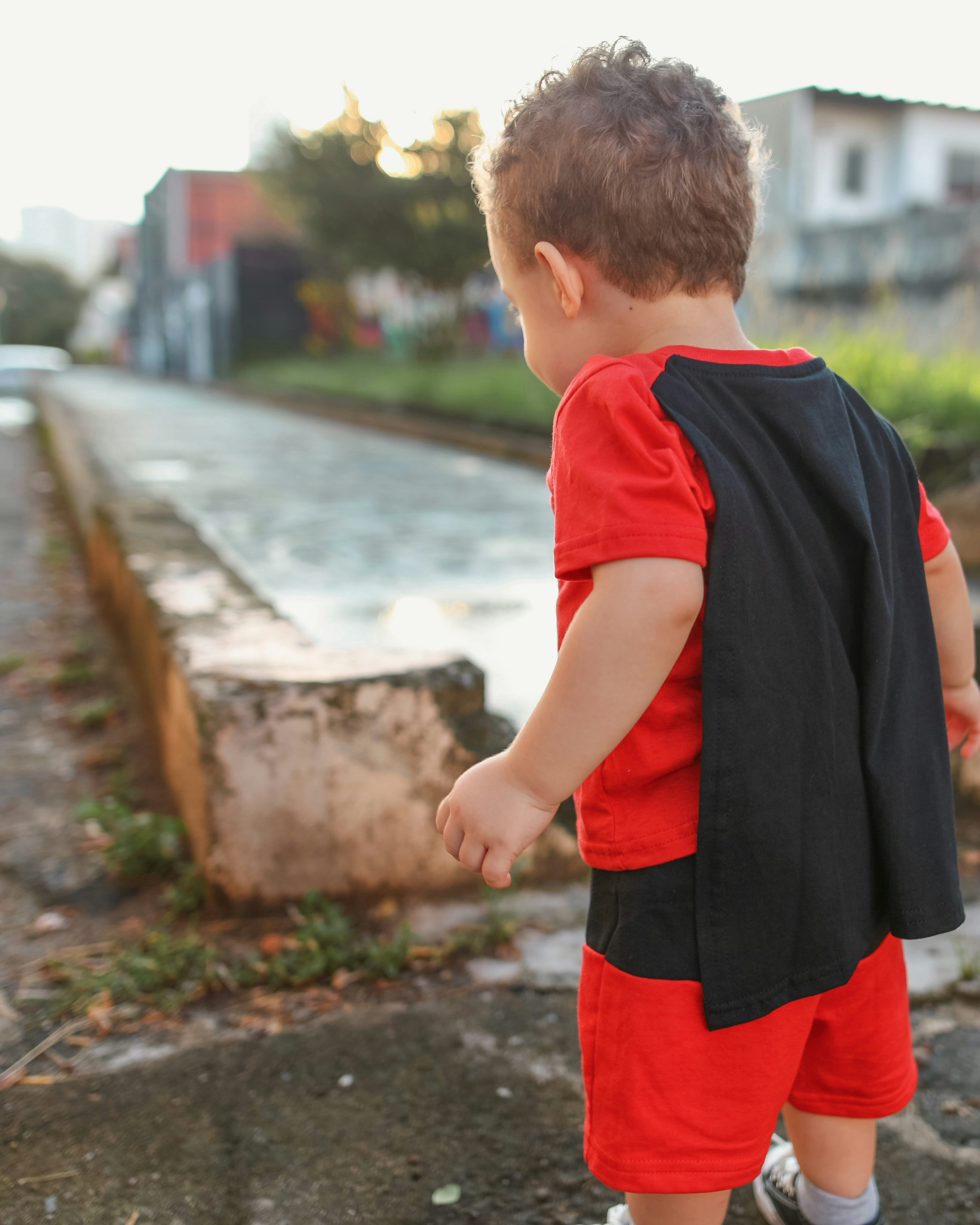 Little boy in a superhero costume stands outside.