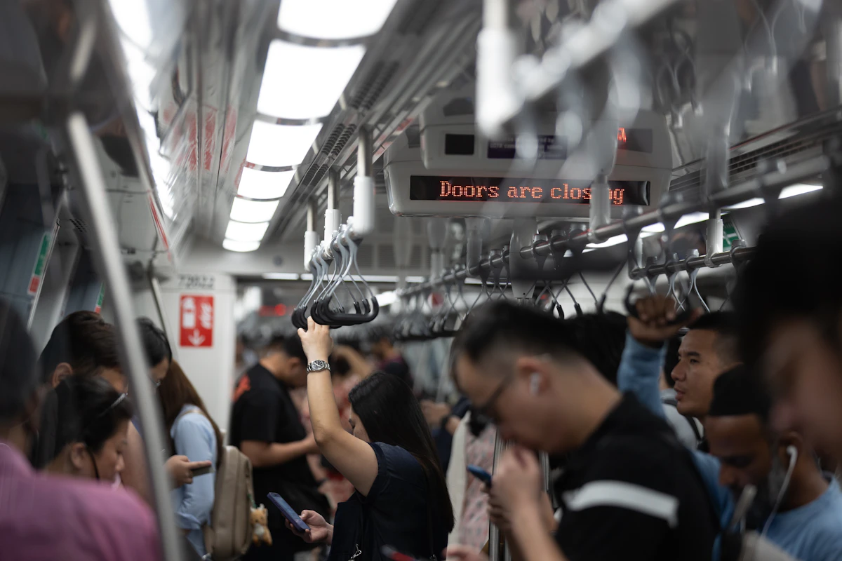 Commuters standing pressed together on a crowded metro train, phones in hand, on the ride back into a full-time office routine