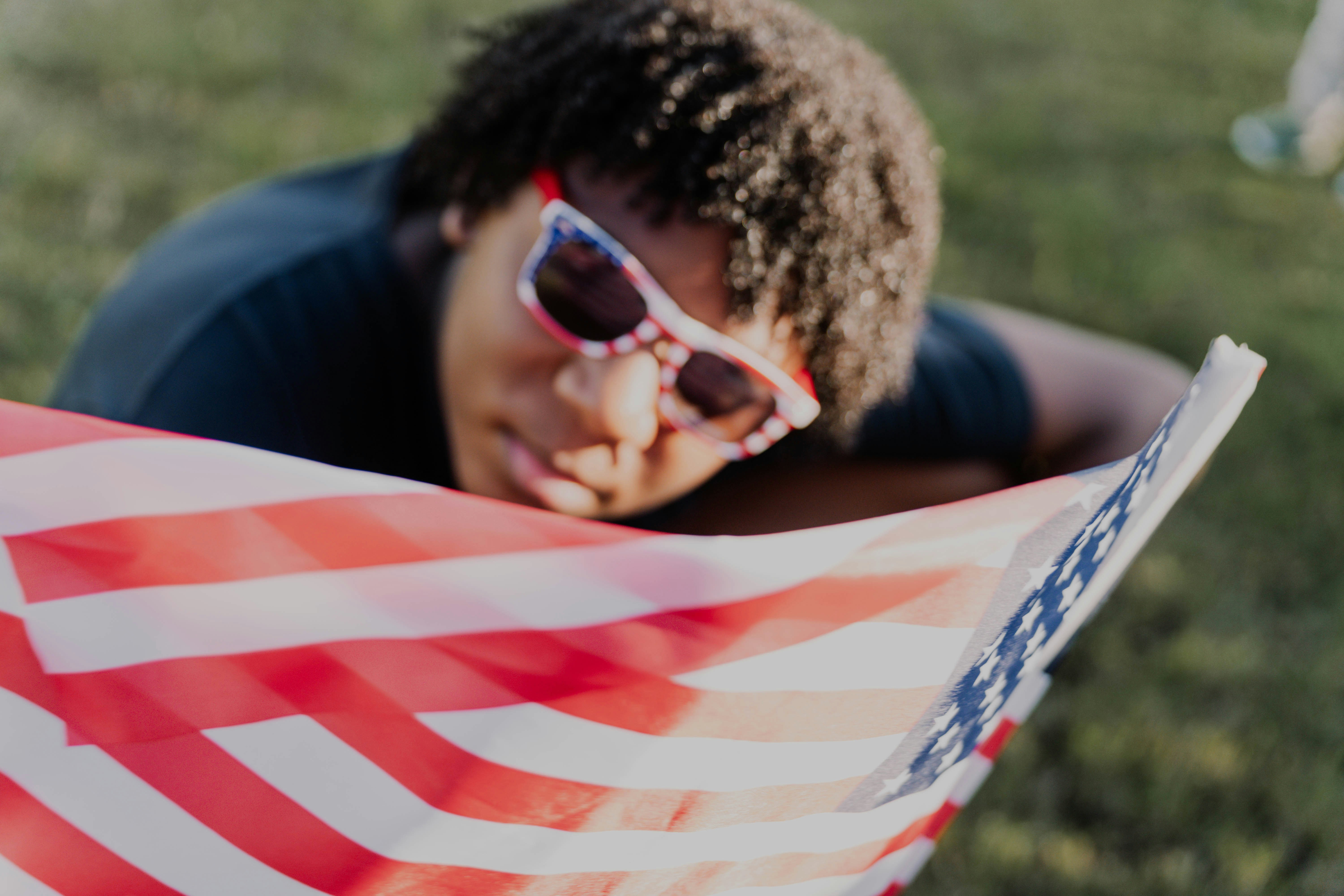 Person wearing shades rests near an american flag.