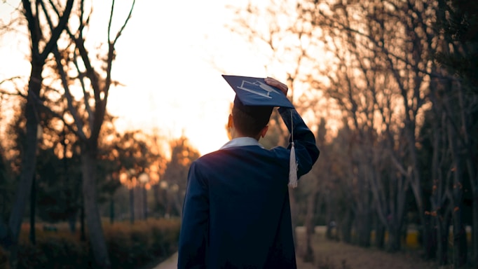 Graduating student celebrates on a path at sunset.