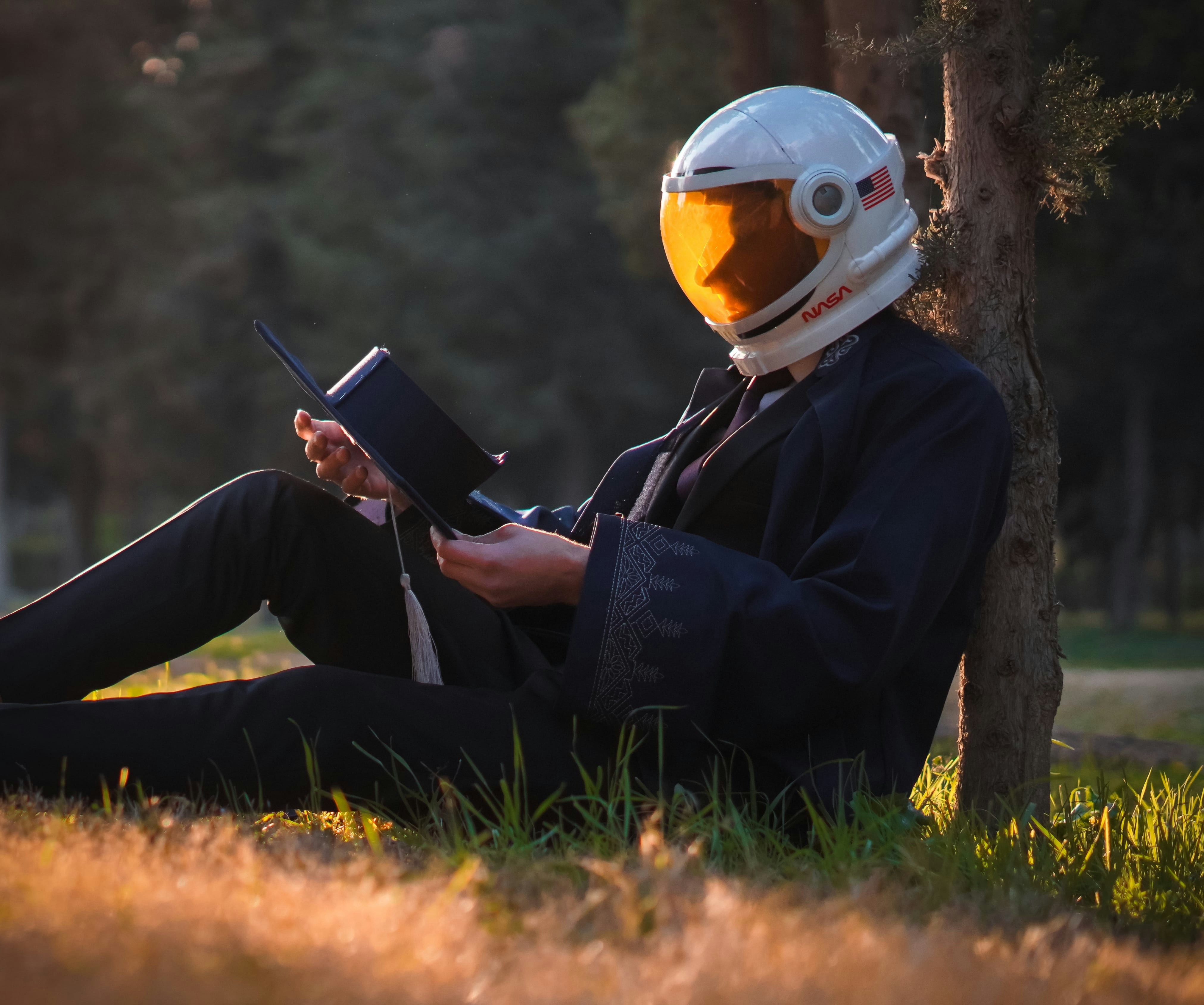 Astronaut reads a book while relaxing in the park.