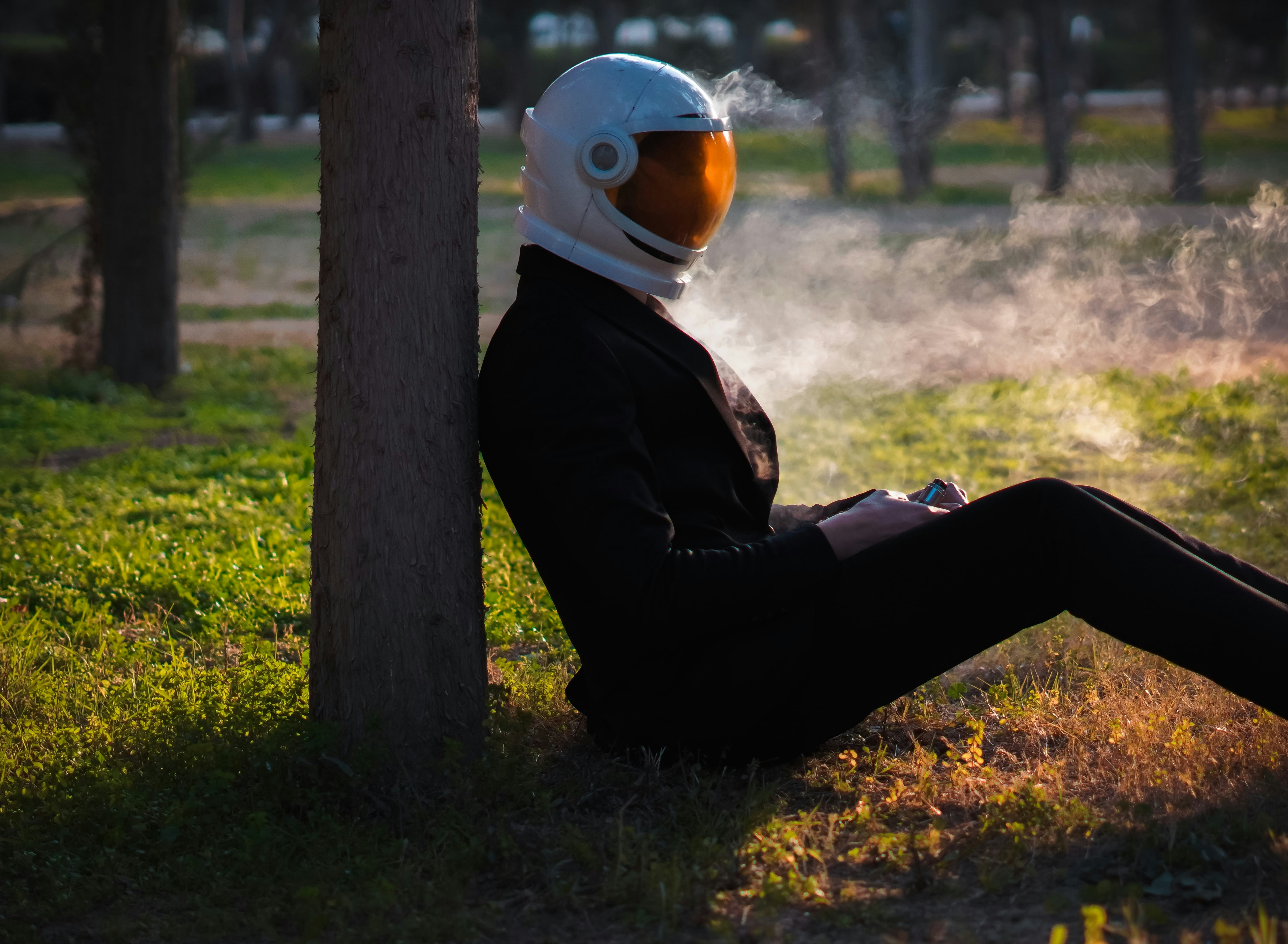 Person in a helmet rests against a tree.