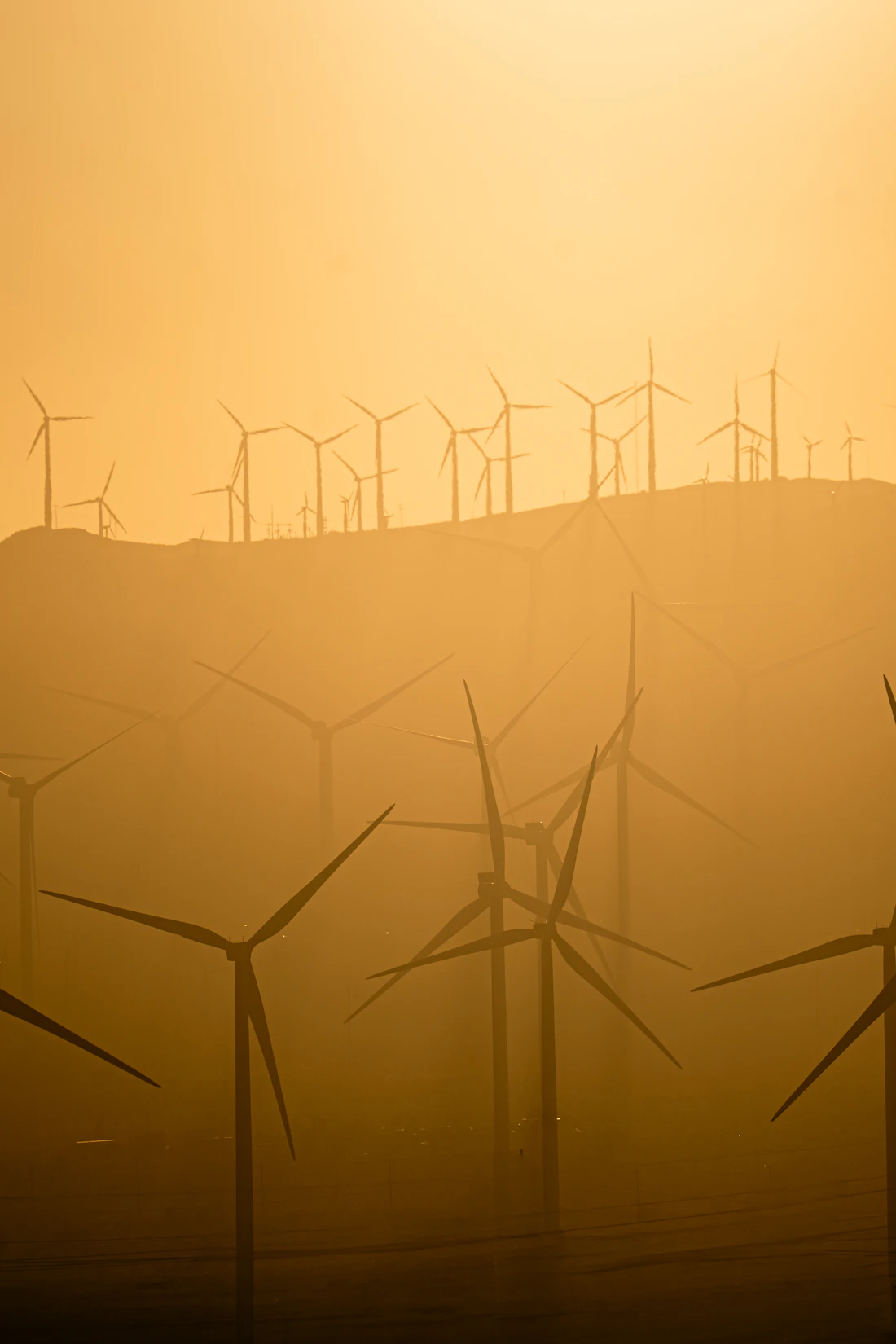 Wind turbines on hills under a hazy golden sky.