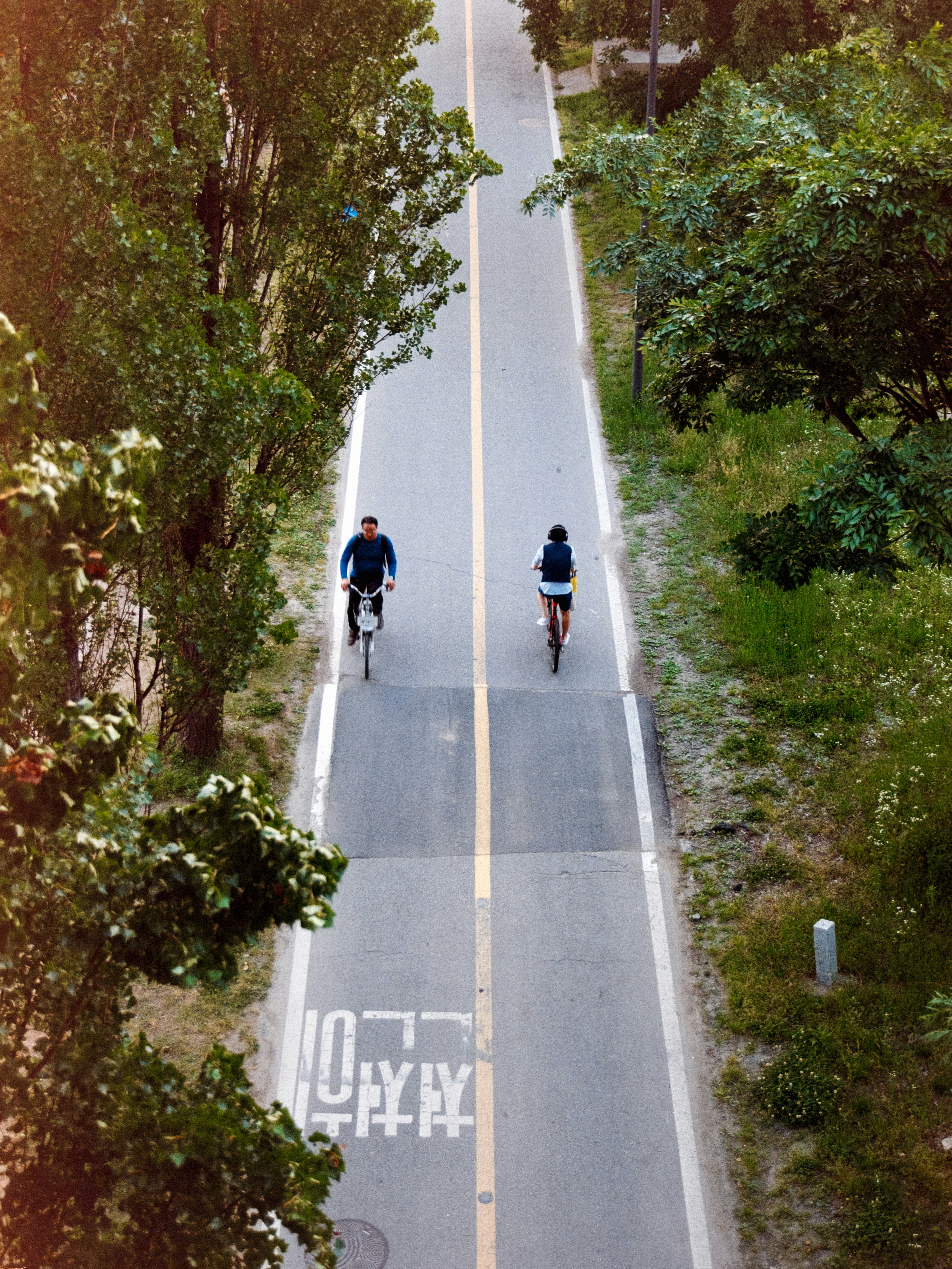 Two people ride bikes down a paved path.