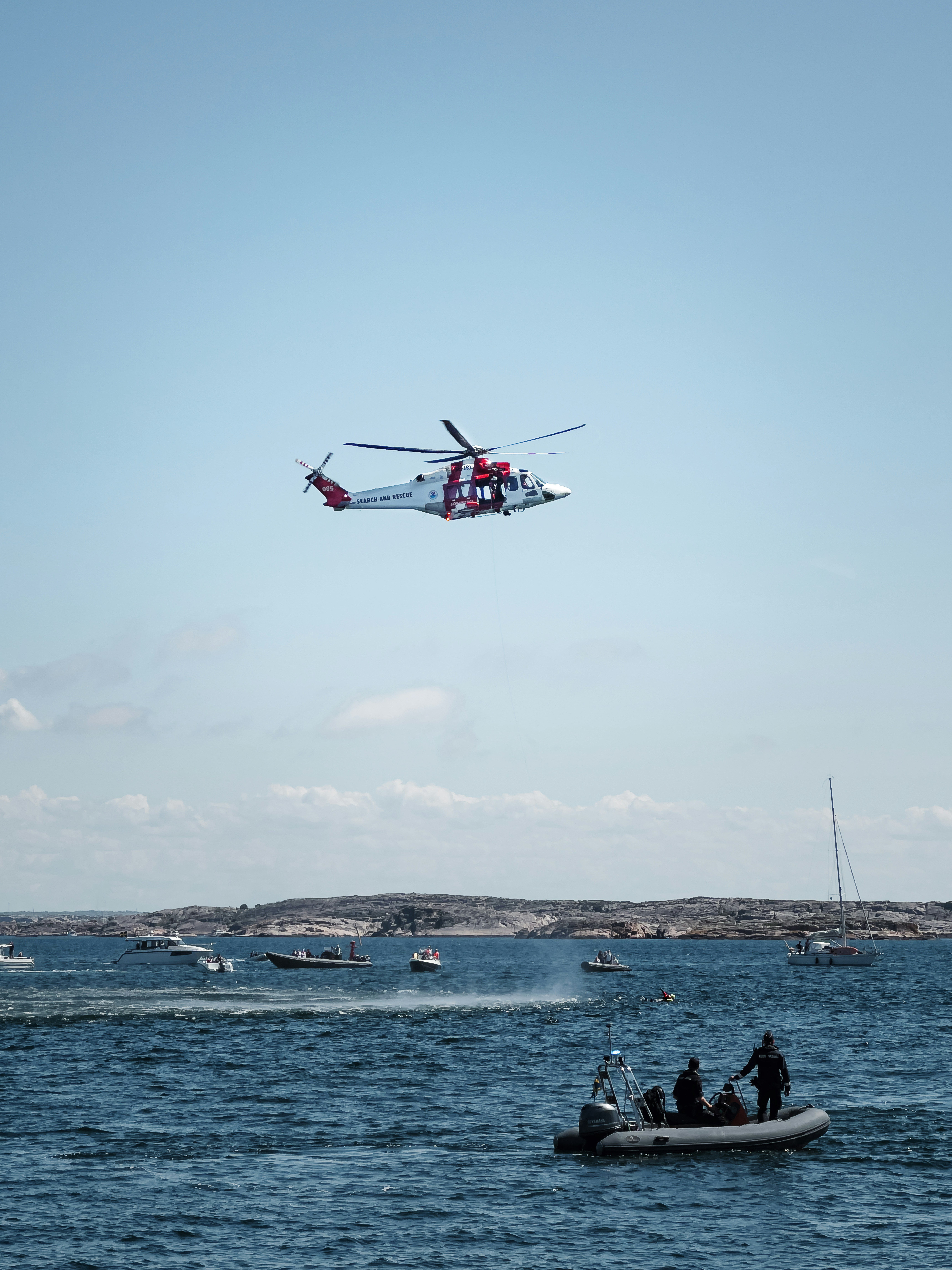 A helicopter flies over the ocean with rescue boats.