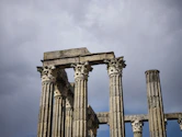 Ancient roman columns stand against a cloudy sky.