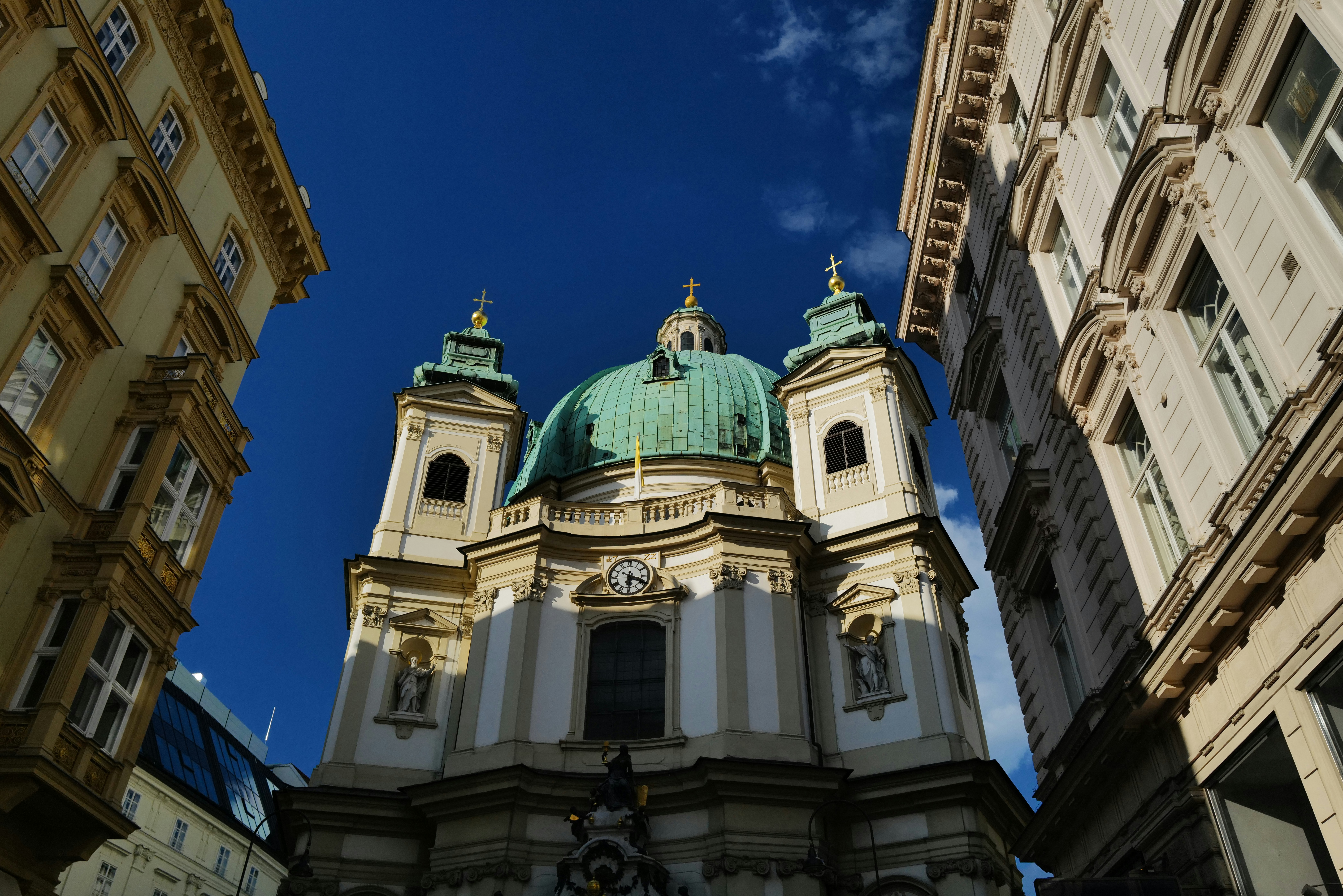 A church stands between buildings against a blue sky.
