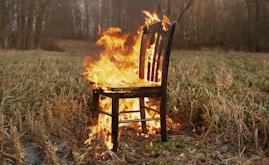 A chair burns fiercely in a field.