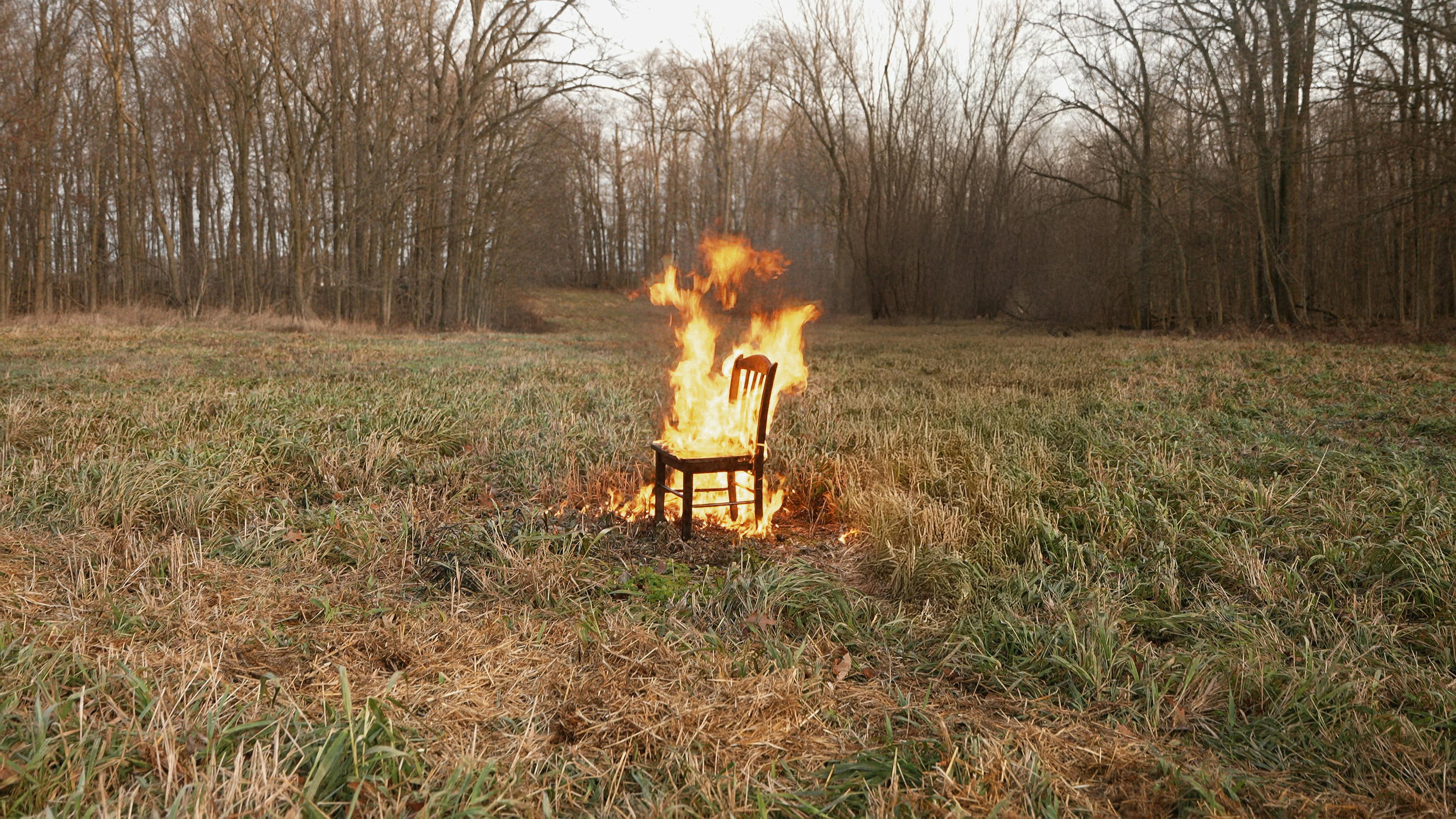 A burning chair sits alone in a field.