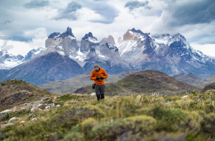 A lone walker crossing scrubland beneath snow-covered peaks.
