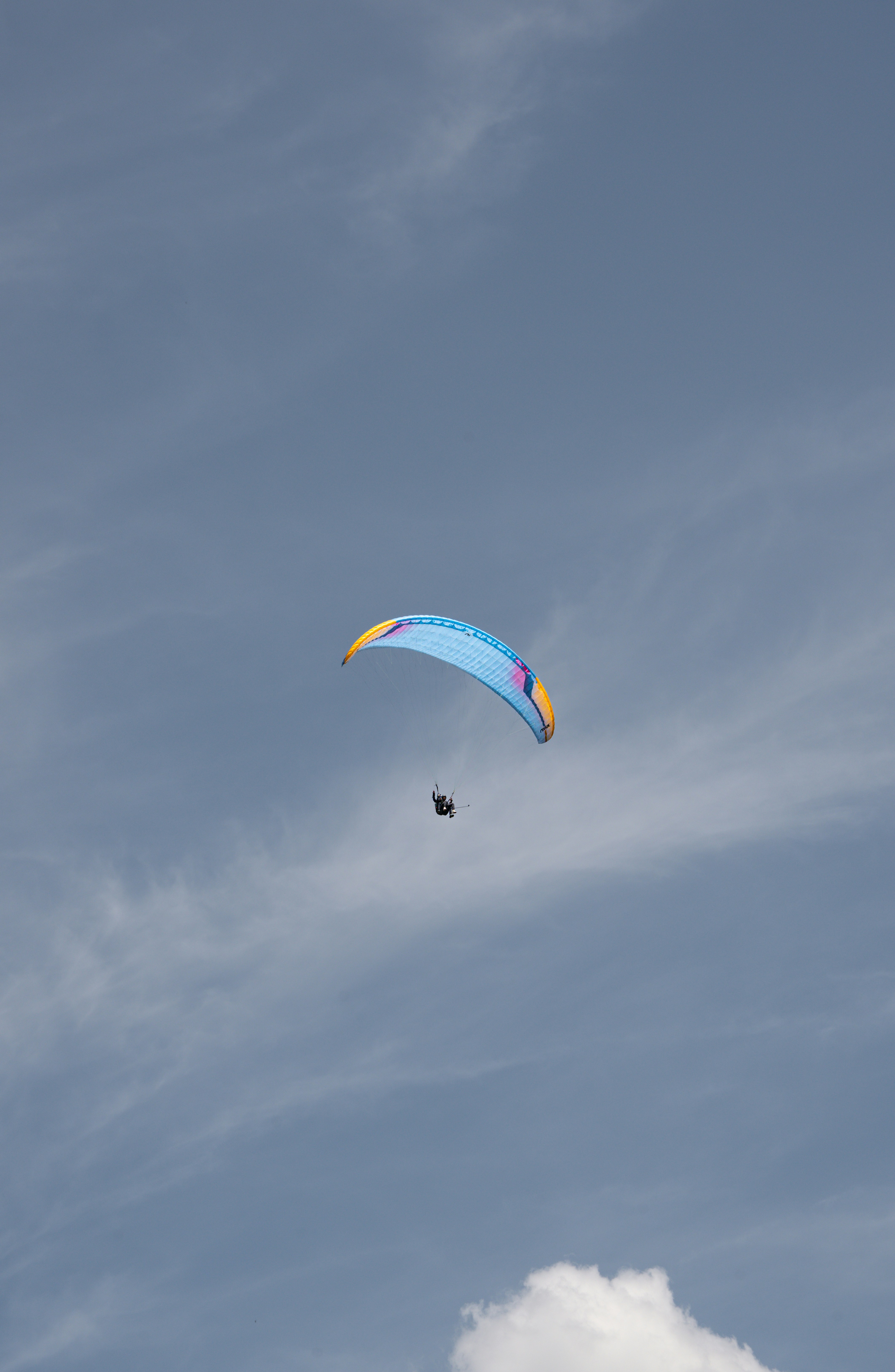 A paraglider soars through the cloudy sky.