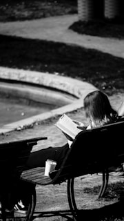 A woman reads a book outdoors on a bench.