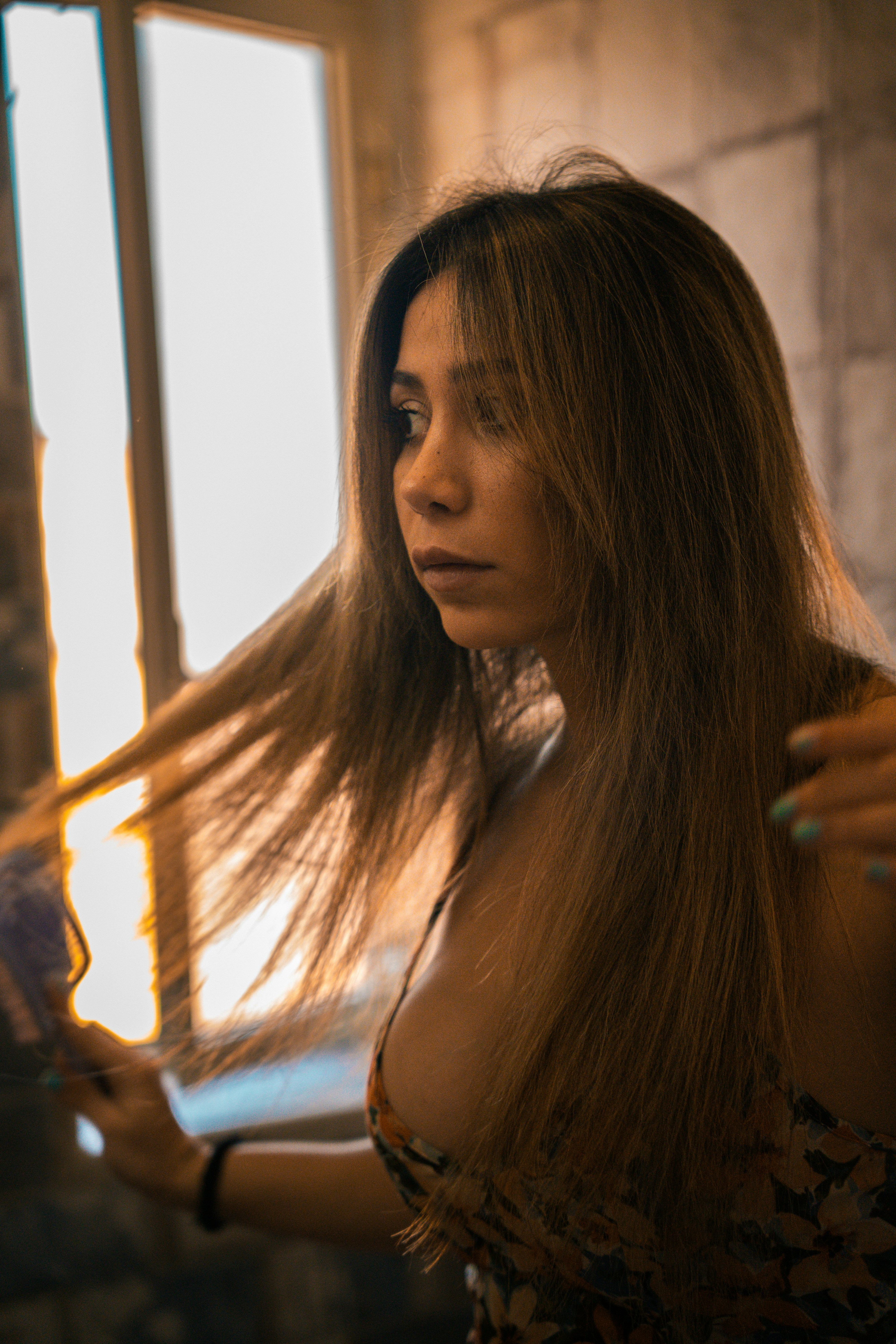 Mujer con pelo largo posa cerca de una ventana.