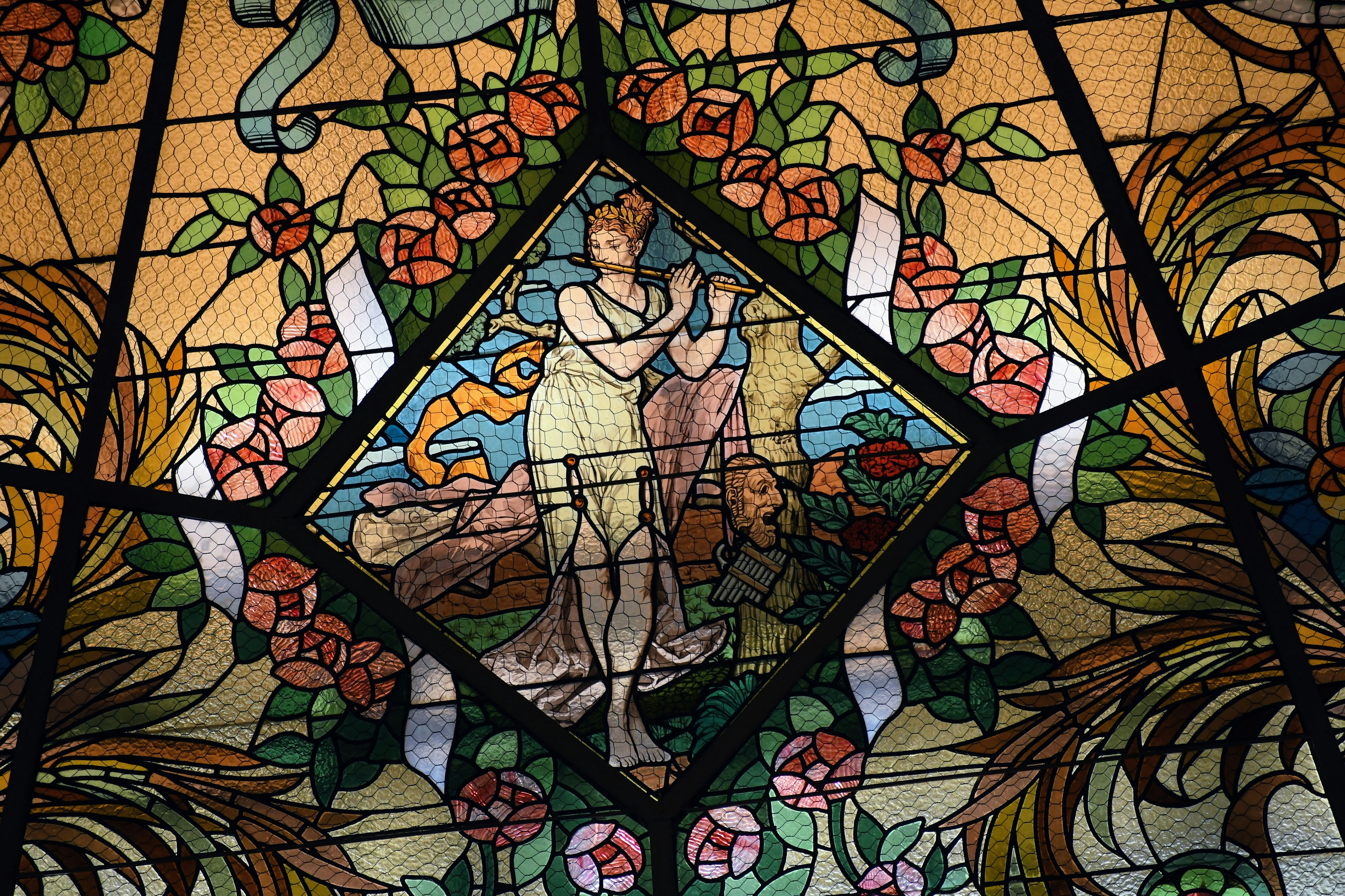 Stained glass panel depicts classical figures and roses.