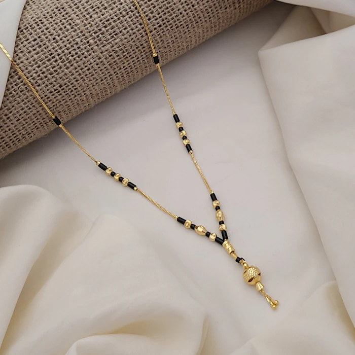 Gold mangalsutra with black beads and a small textured gold pendant on white satin