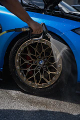 A person is washing a blue BMW car wheel.