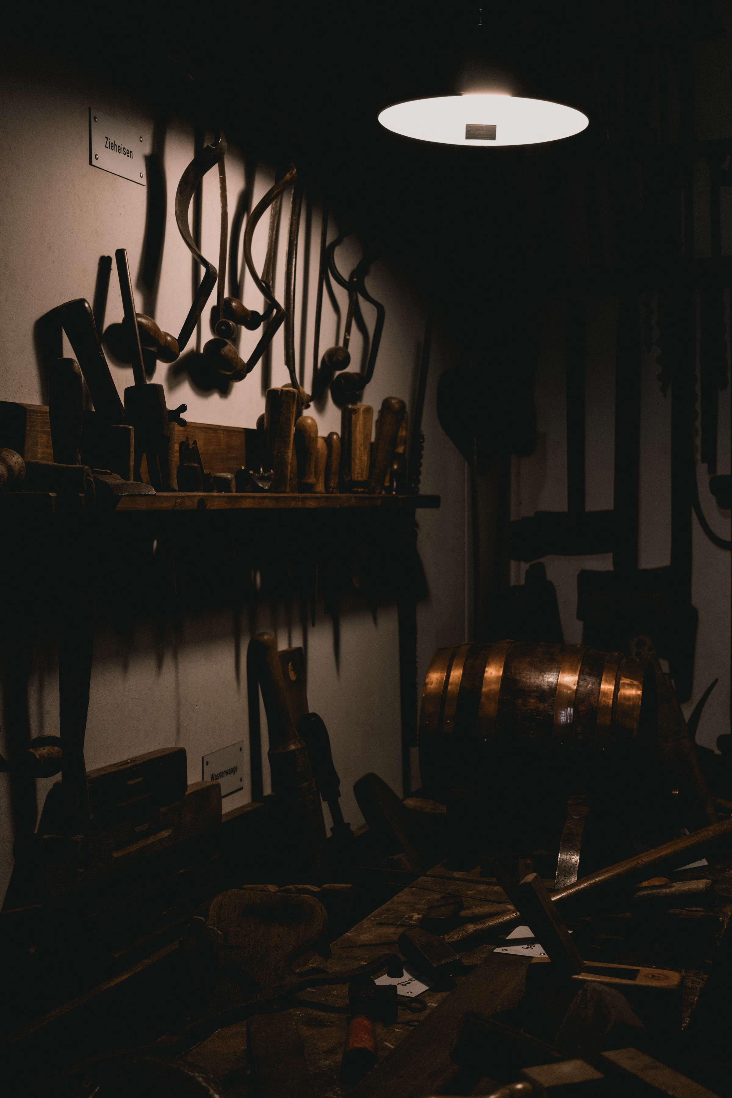 A moody workshop with a wooden workbench, wall-hung hand tools and a single overhead light